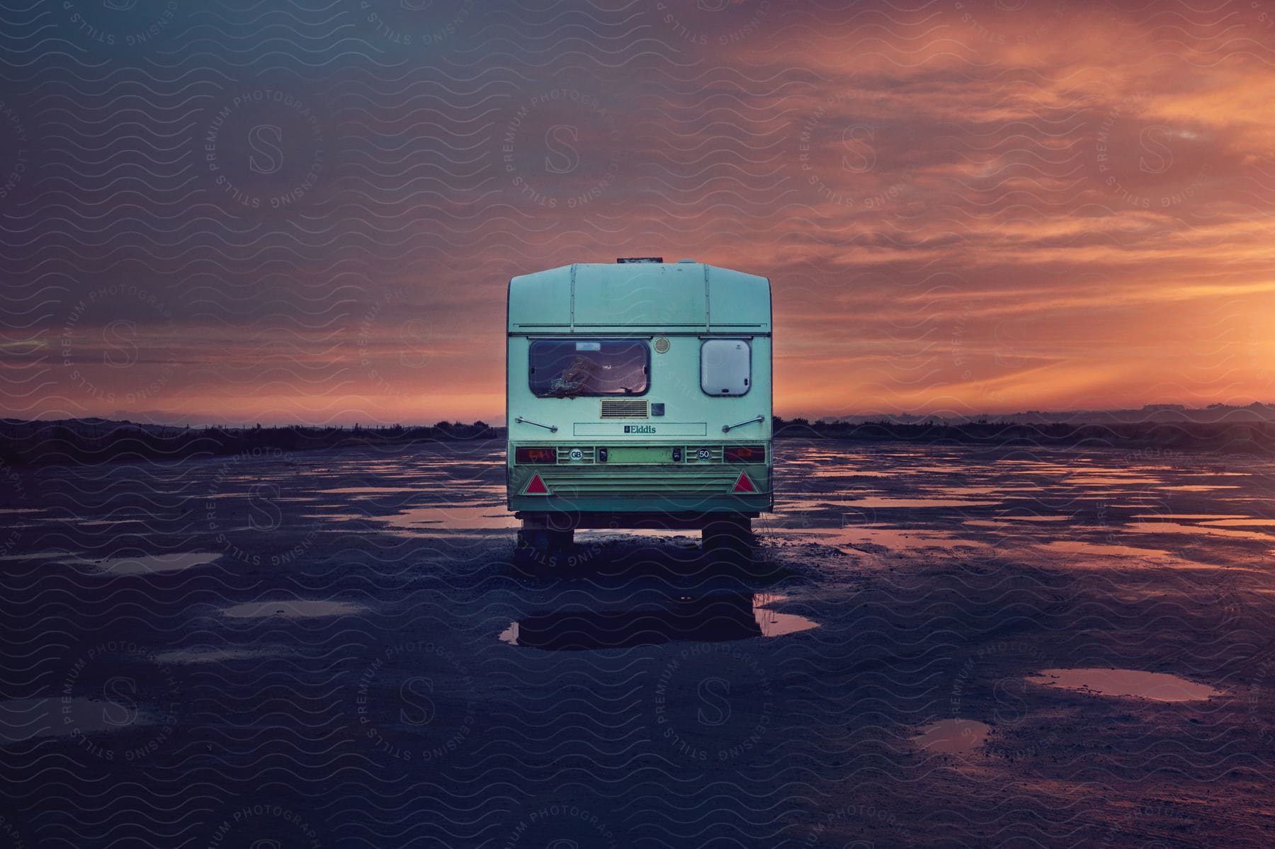 An rv parked by a lake at sunset under a dark and pink sky