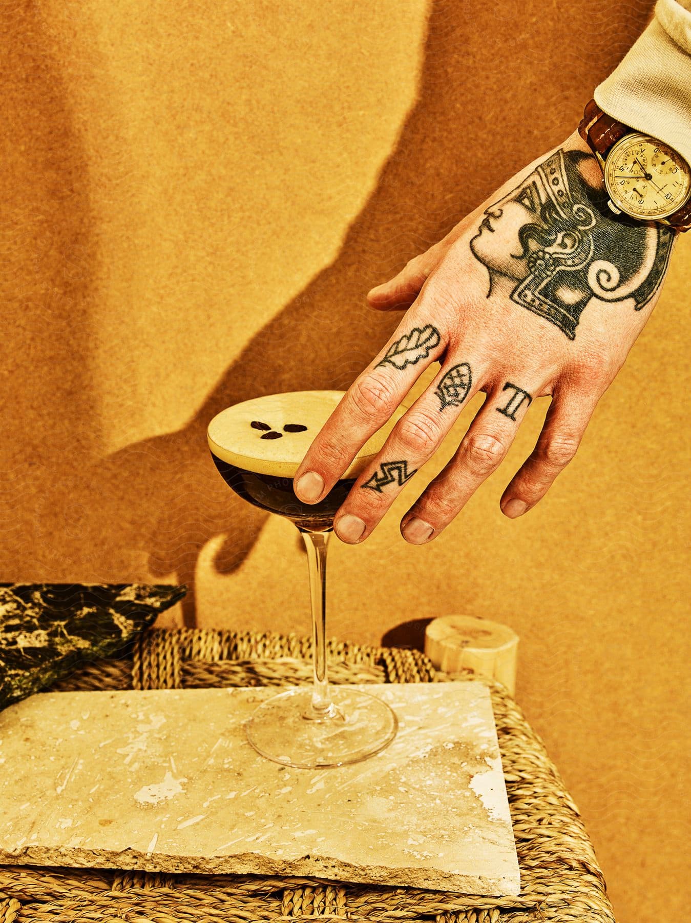 A tattooed mans hand reaching for an espresso martini cocktail