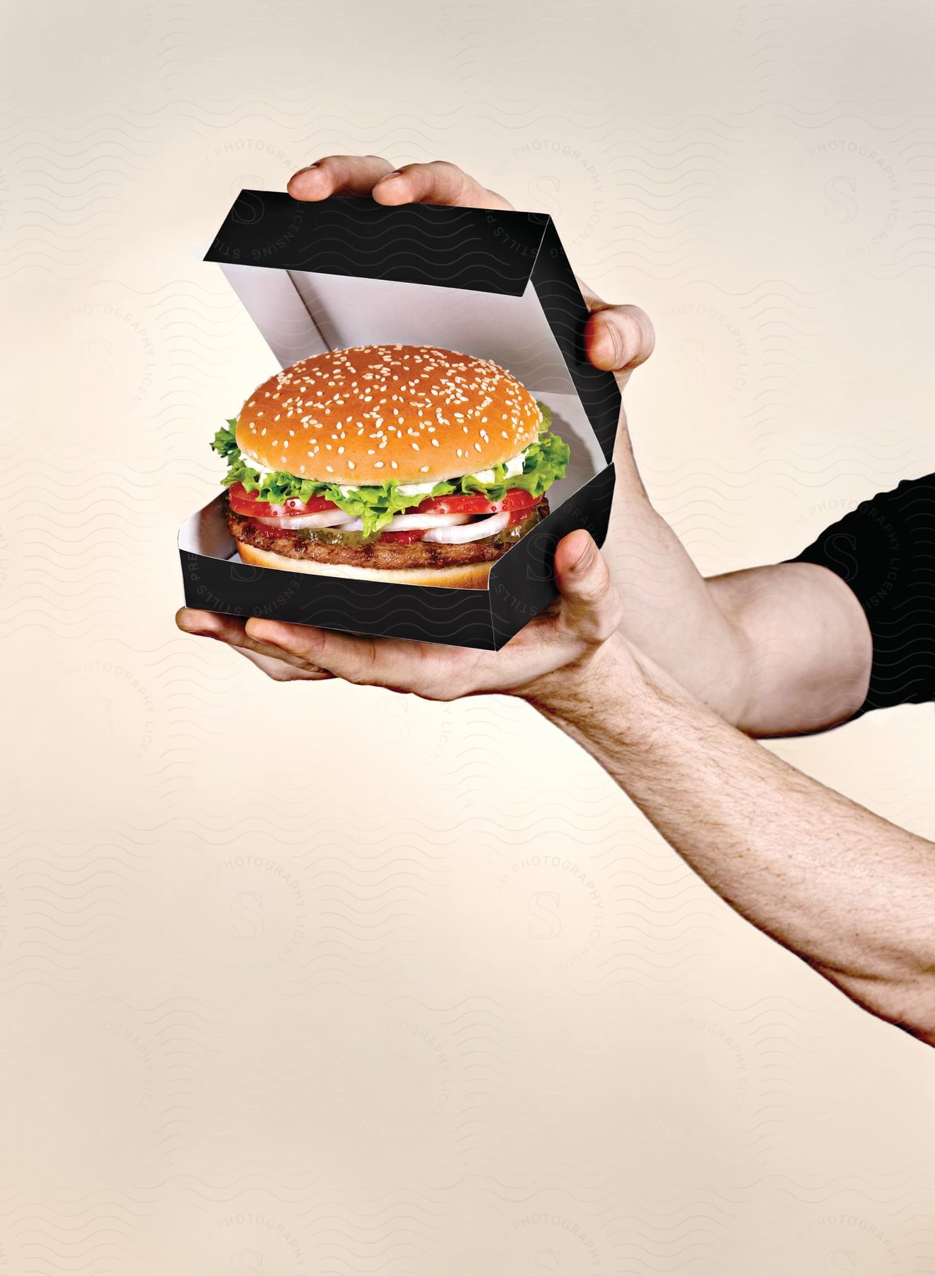 A pair of hands holding a hamburger in a black box