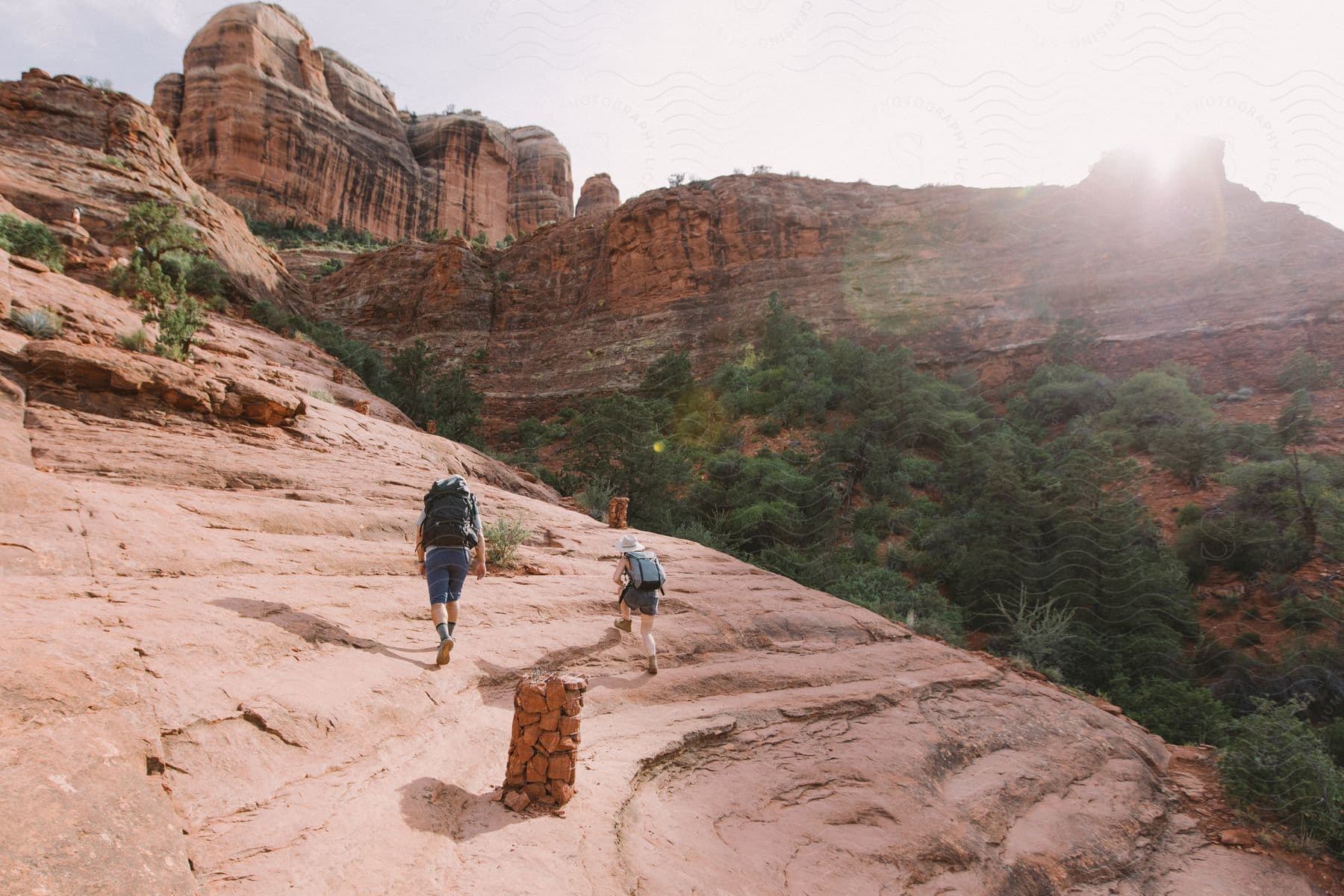 Two individuals hike up a mountain side while carrying backpacks