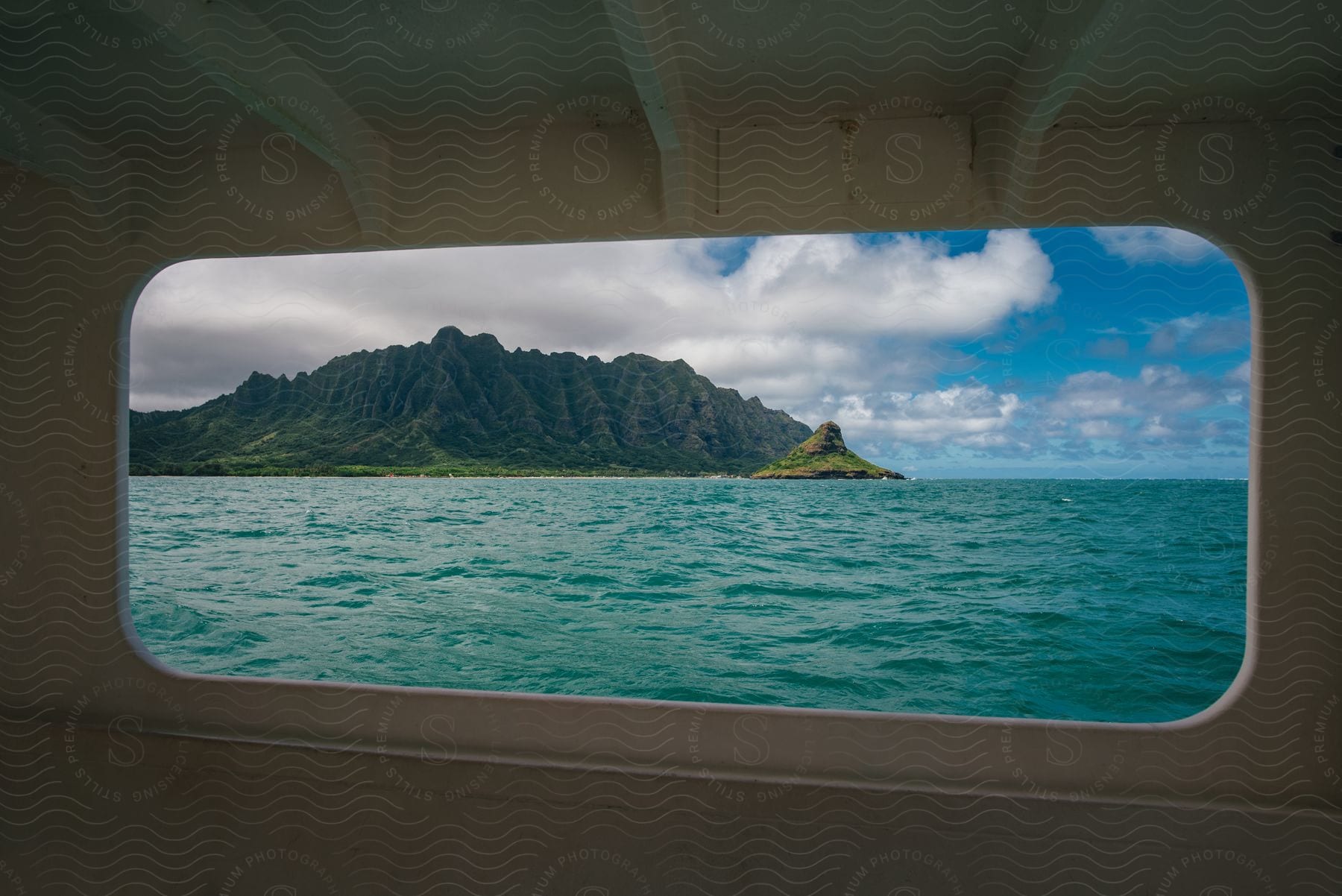 Jagged mountain island and blue water under a blue sky with white fluffy clouds on a sunny day