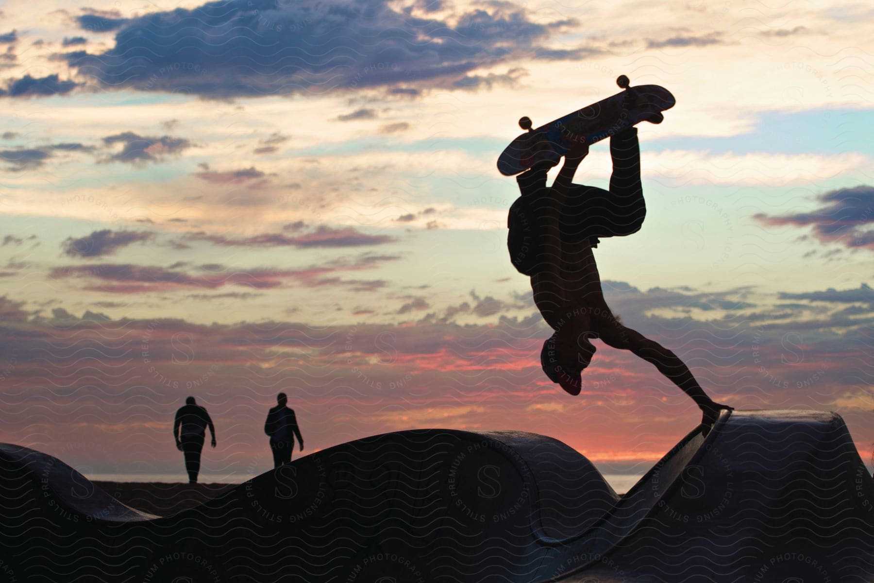 A young man performing a skateboarding trick on a skate park during sunset