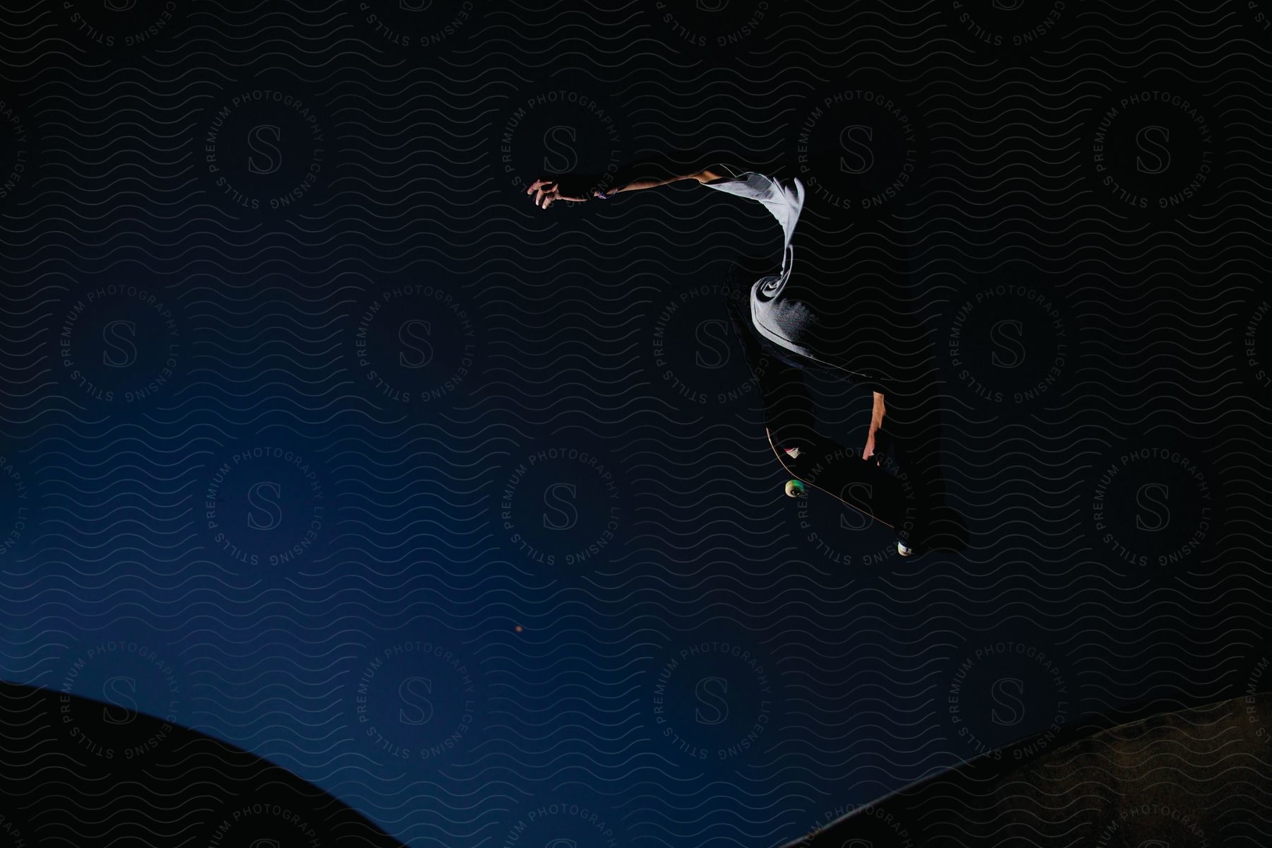 A man is seen performing a skateboard trick in midair after launching from a skate ramp at night