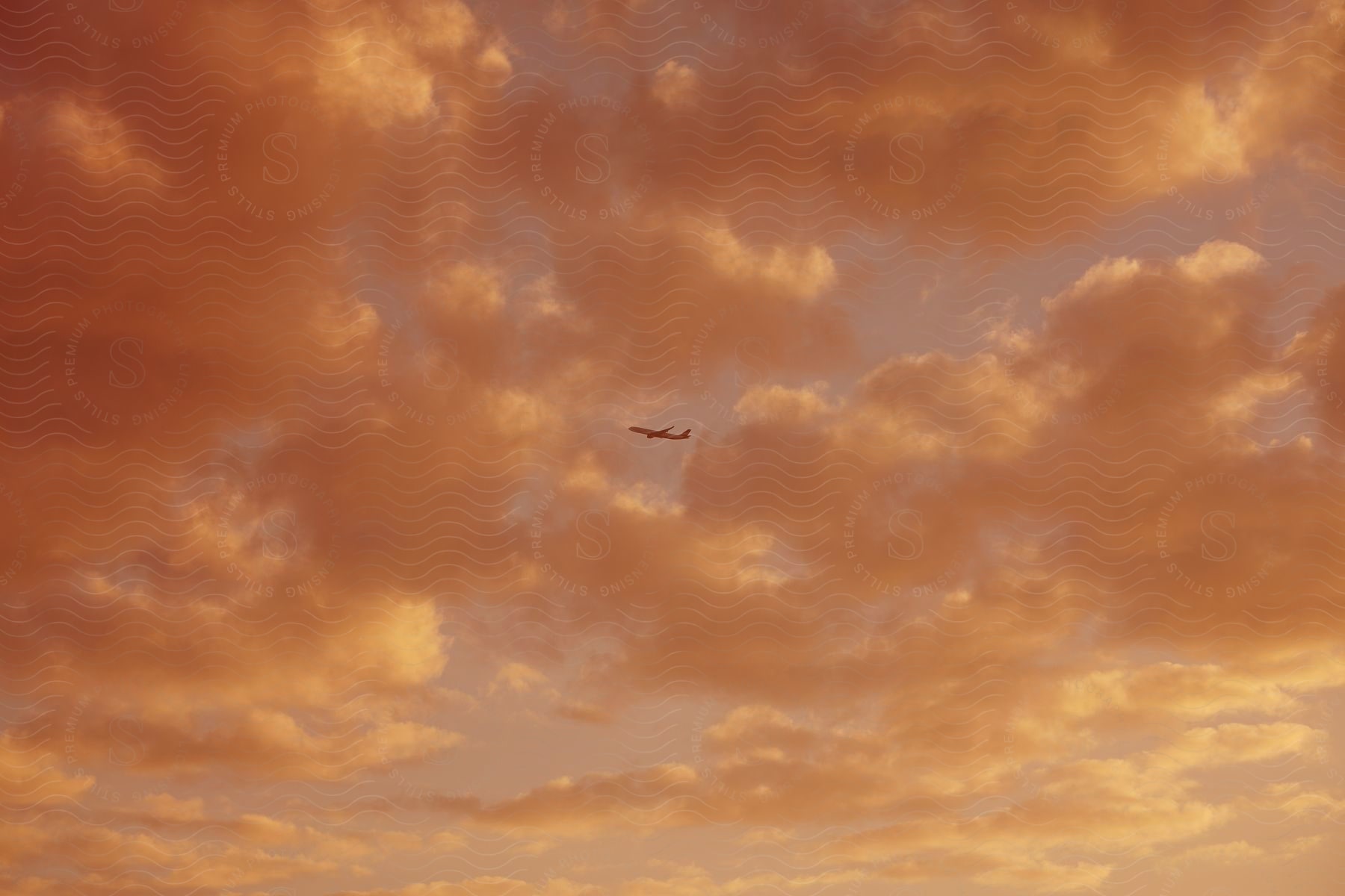 A commercial airplane flies through the cloudy sky at dusk