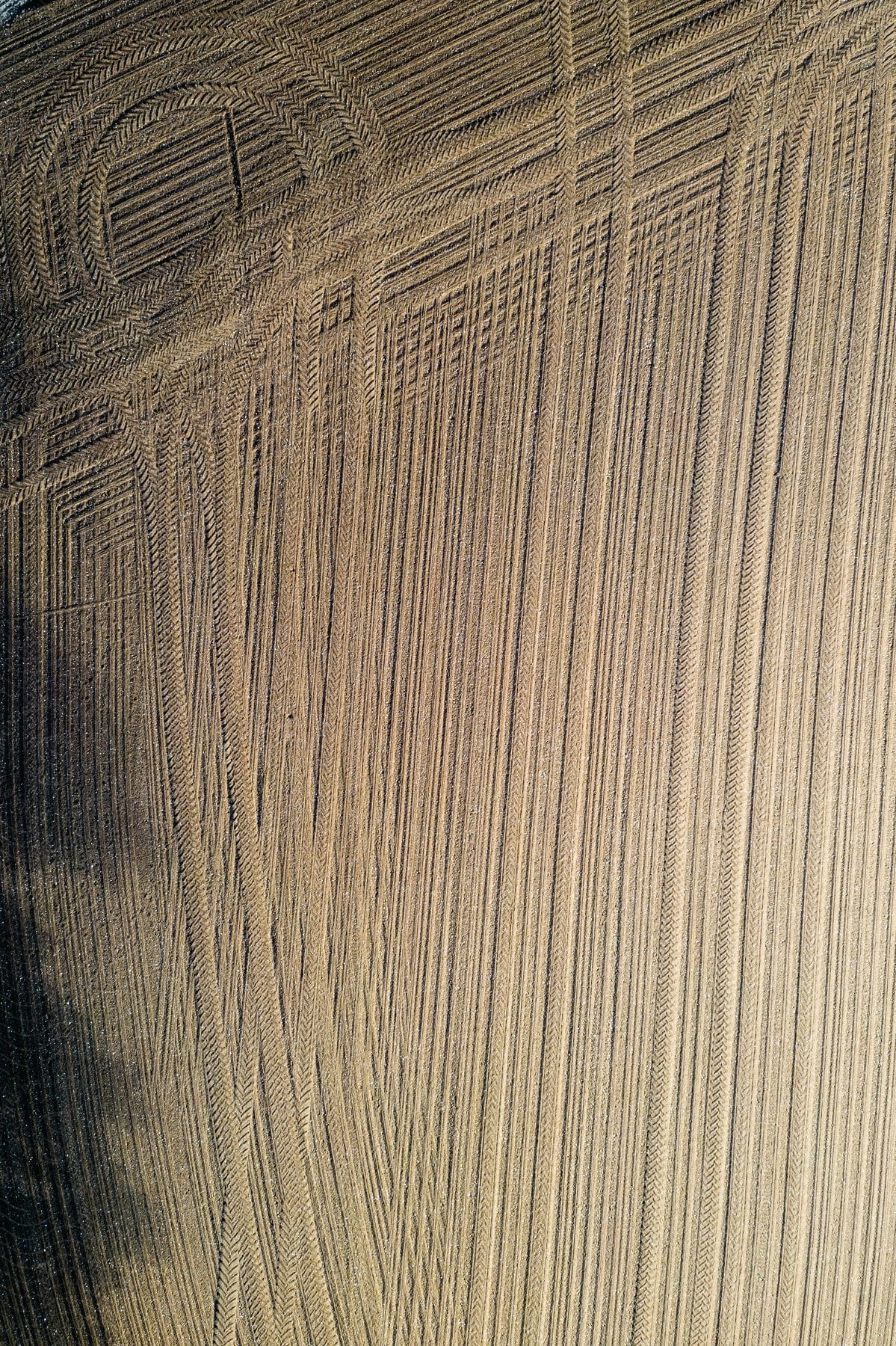 Aerial view of a freshly plowed farm field with crisscrossing tire tracks on brown soil