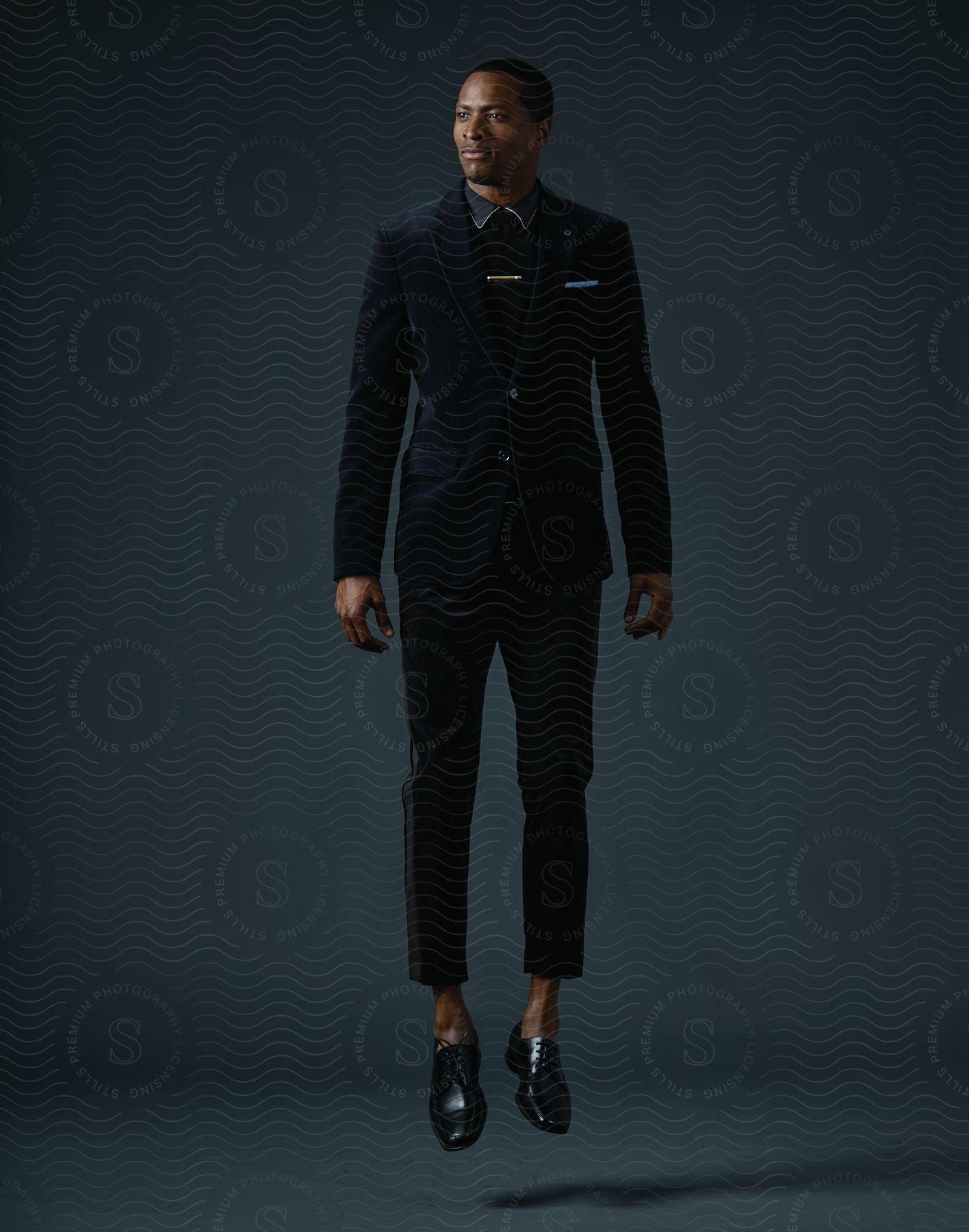 A black man wearing a suit and formal clothing levitating a few inches above the floor