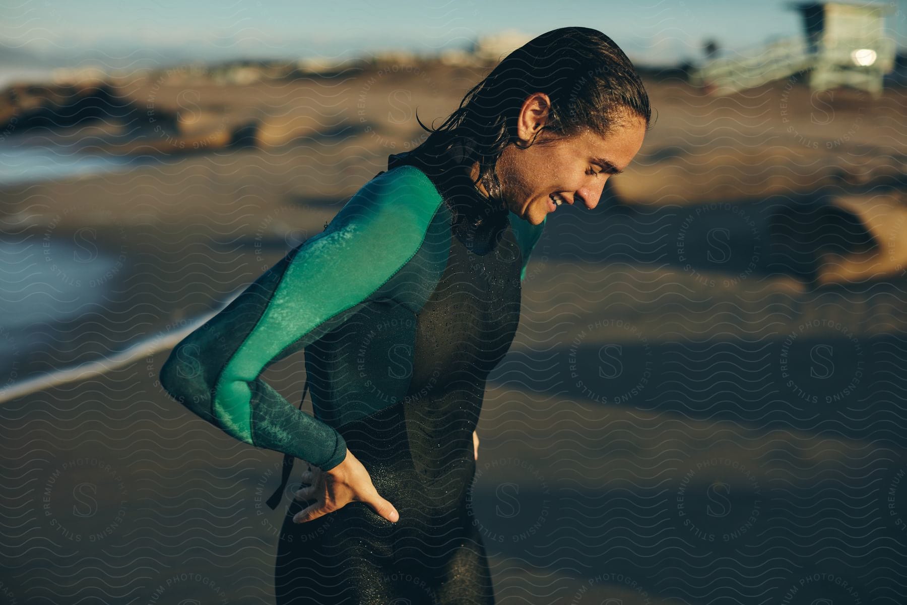 A woman smiles on the beach wearing a wet suit