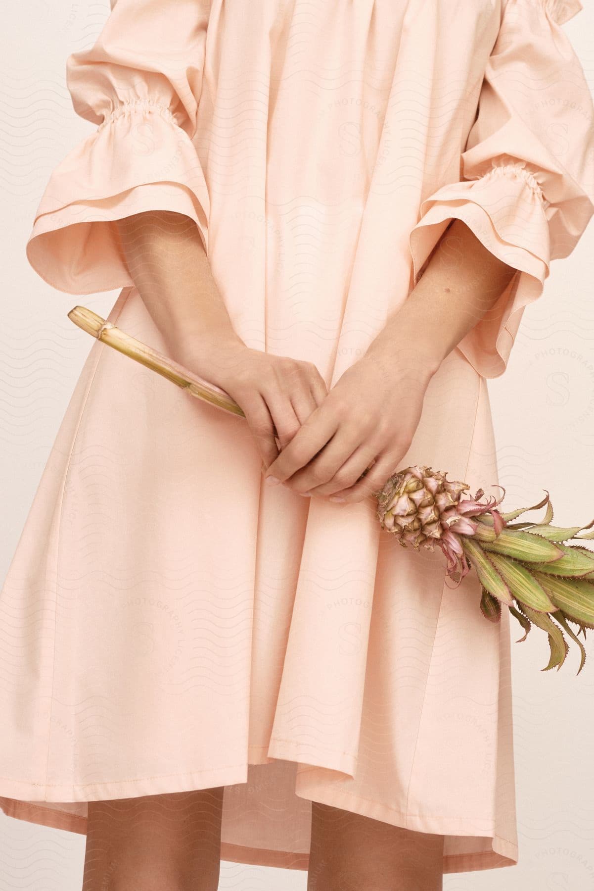 A woman in a pink dress holds a small pineapple on a stem