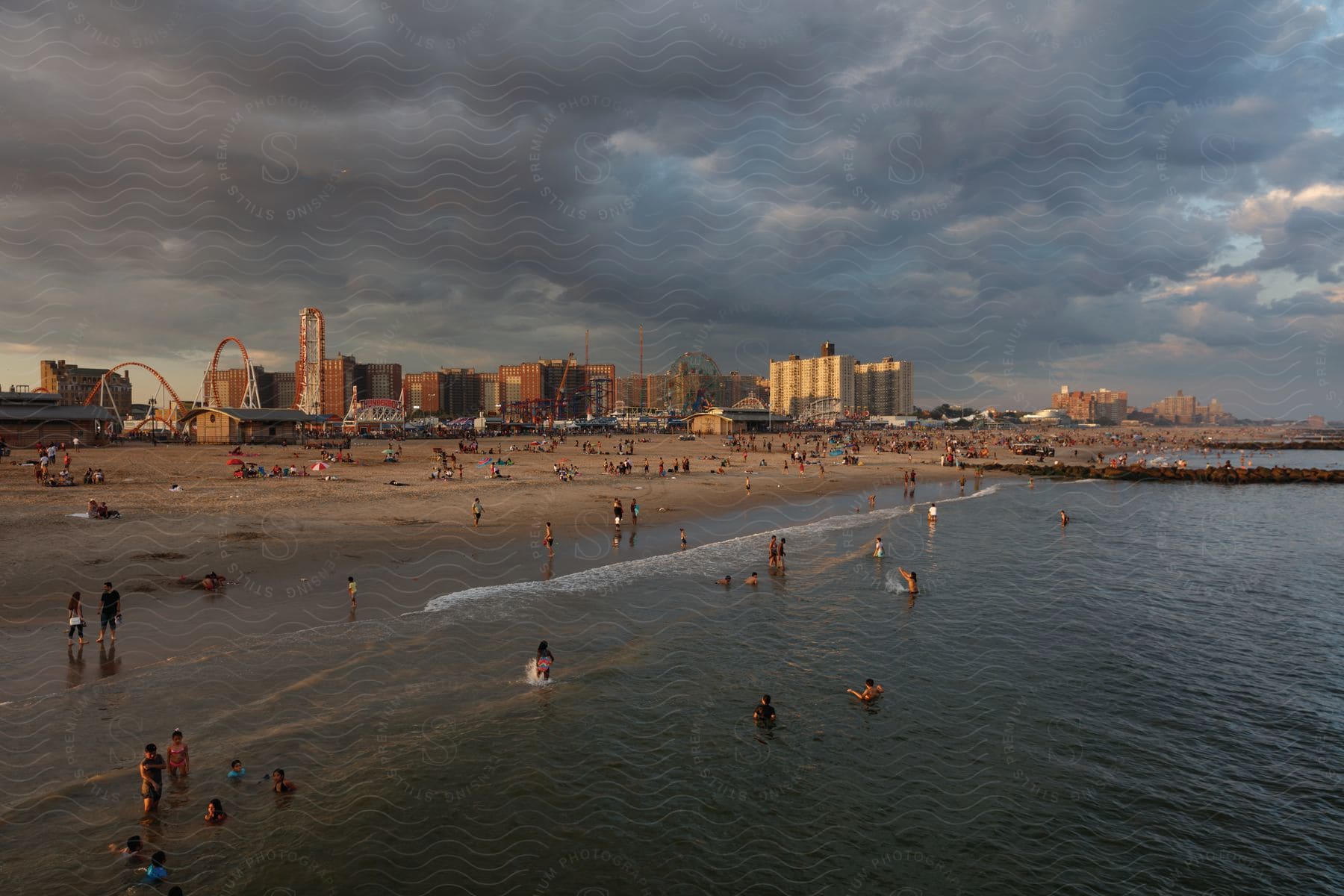 People enjoying the beach behind an amusement park in a big city on a cloudy day