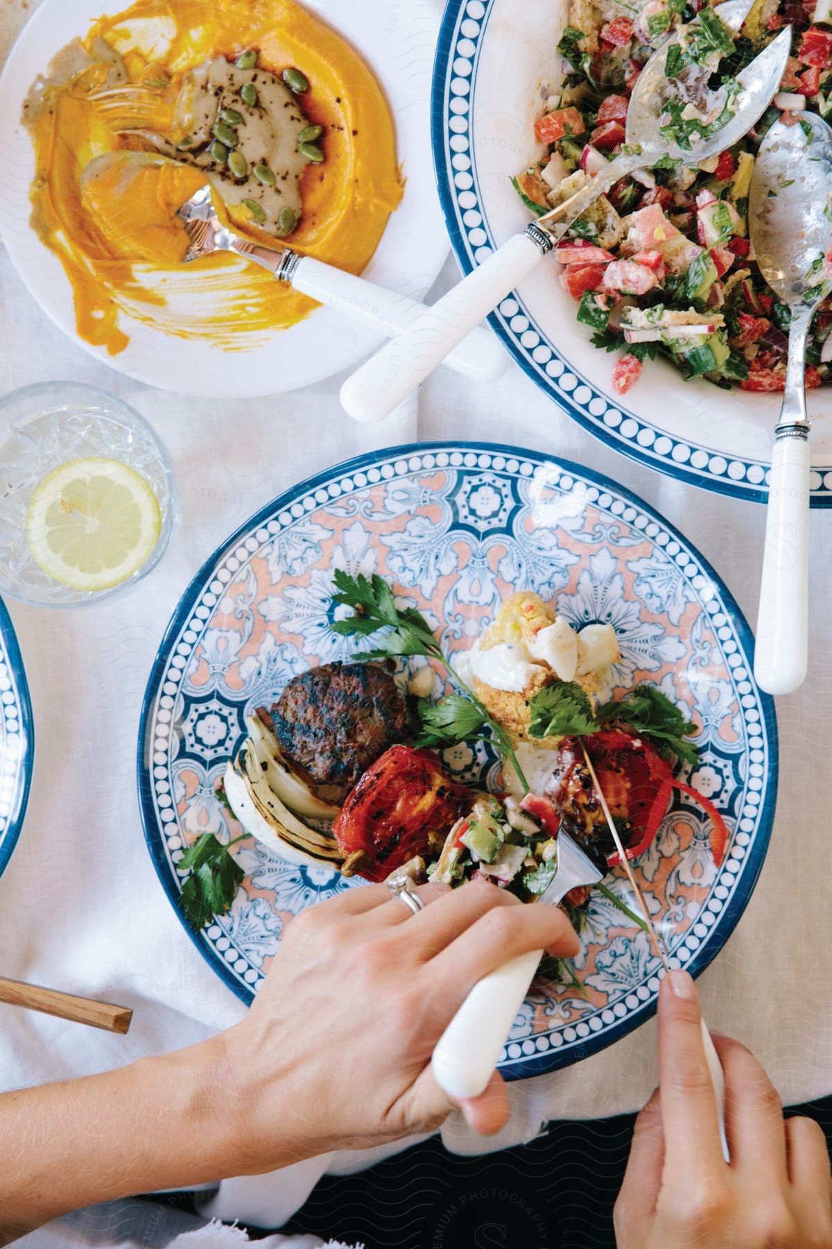 Woman cutting food on a porcelain plate at a set table with a bowl of vinaigrette and traditional food