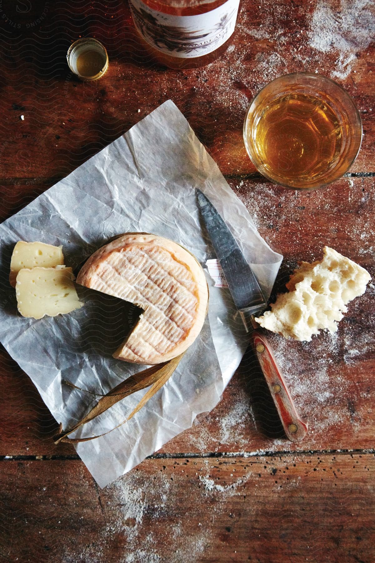 A wheel of cheese a hunk of bread and a glass of whiskey