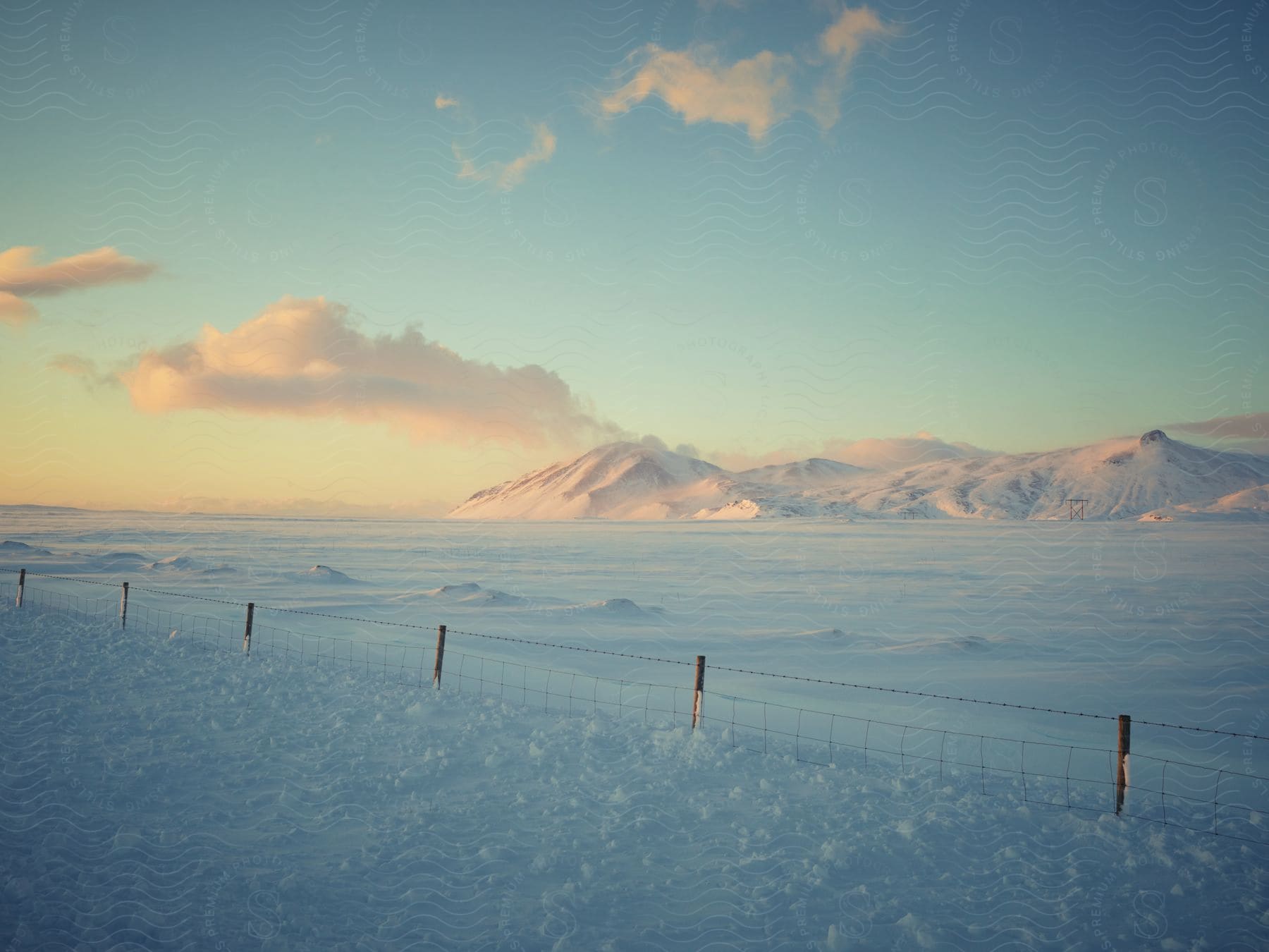 A snowcovered landscape with a short fence and a distant mountain covered in white snow