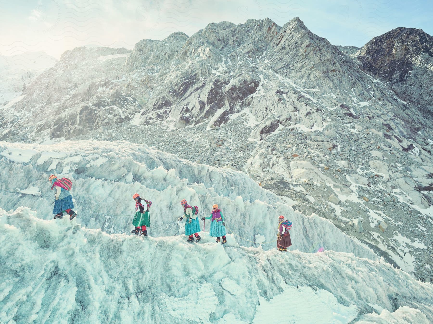 Snowy mountain terrain on a sunny day with five female ice climbers walking on an ice cliff