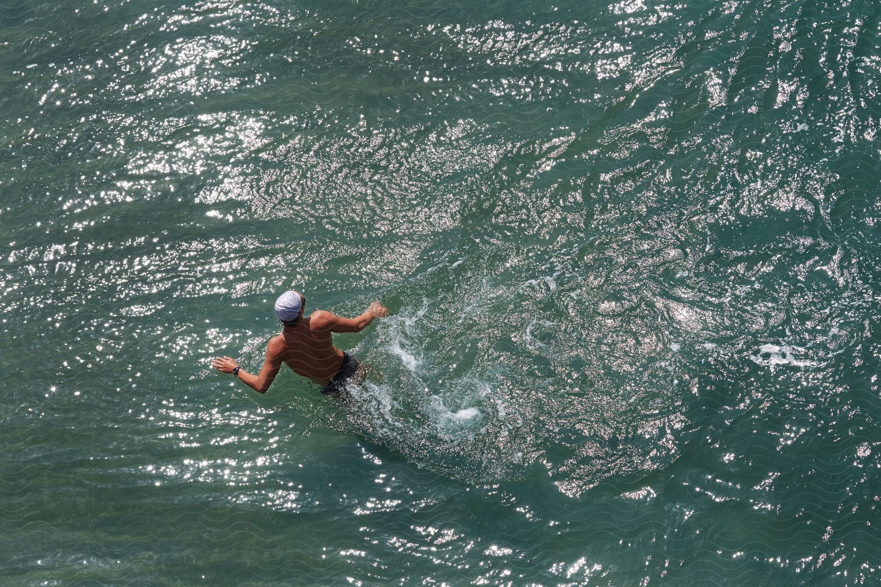 A man in shorts and a swim cap is swimming in the water