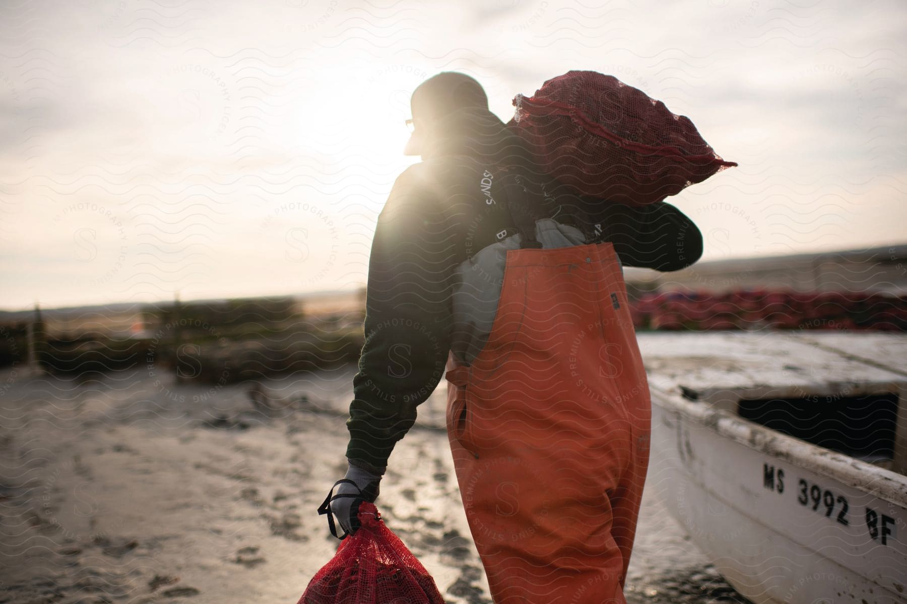 A person carries two bags of crab on a beach near a boat at sunrise