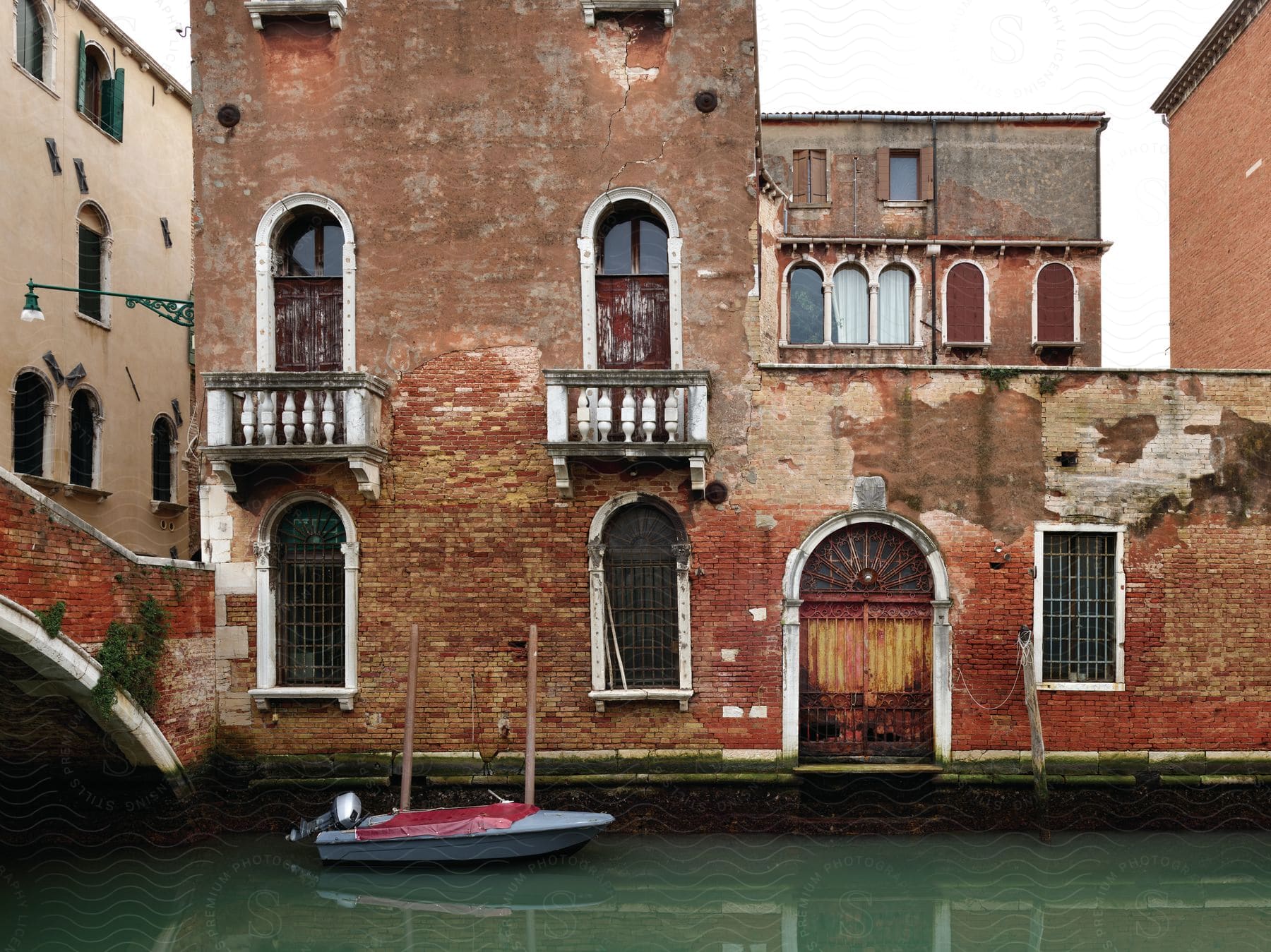 A small motorboat is docked in front of an apartment building near an arched bridge