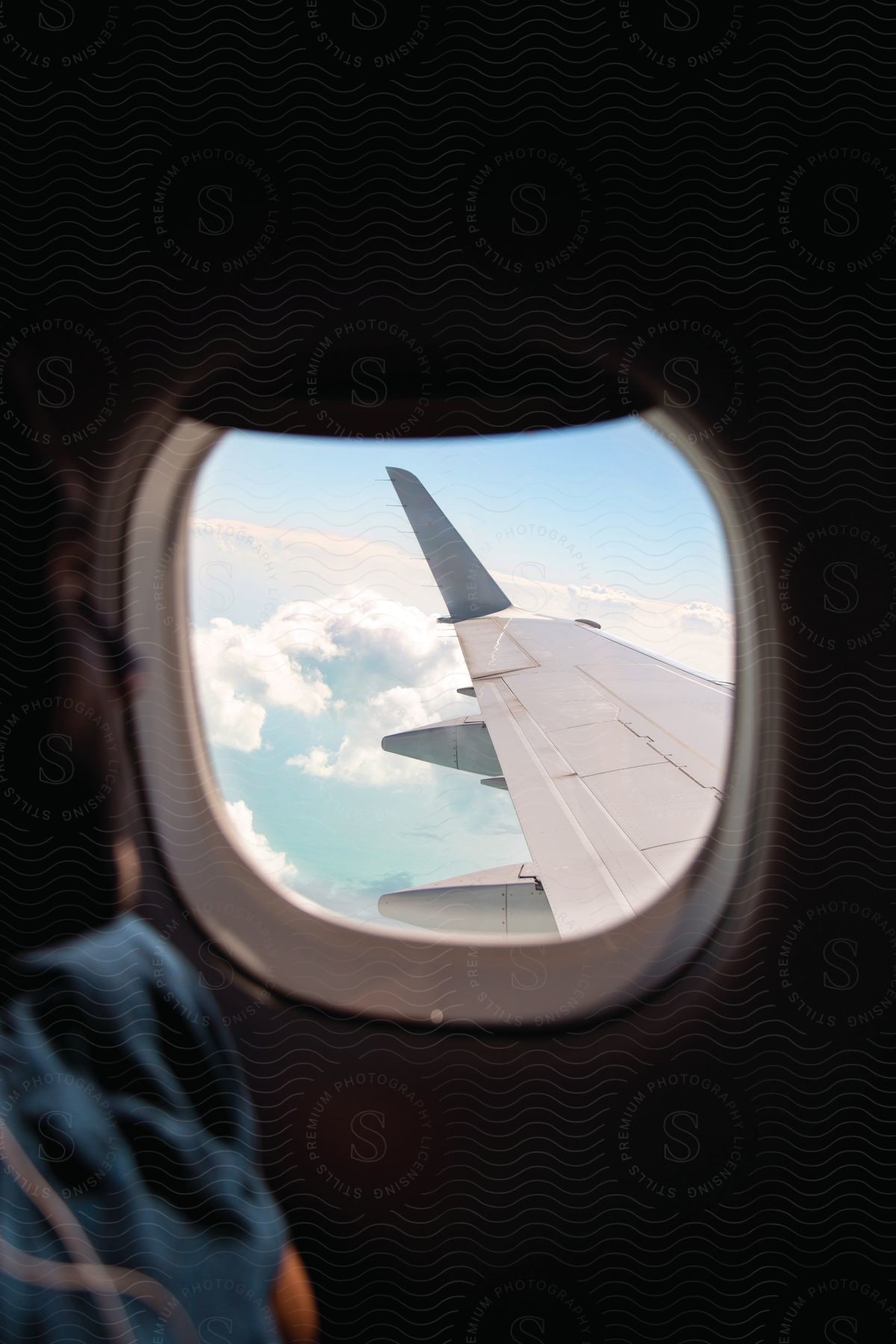 A man looks out of an airplane window at the wing and sky