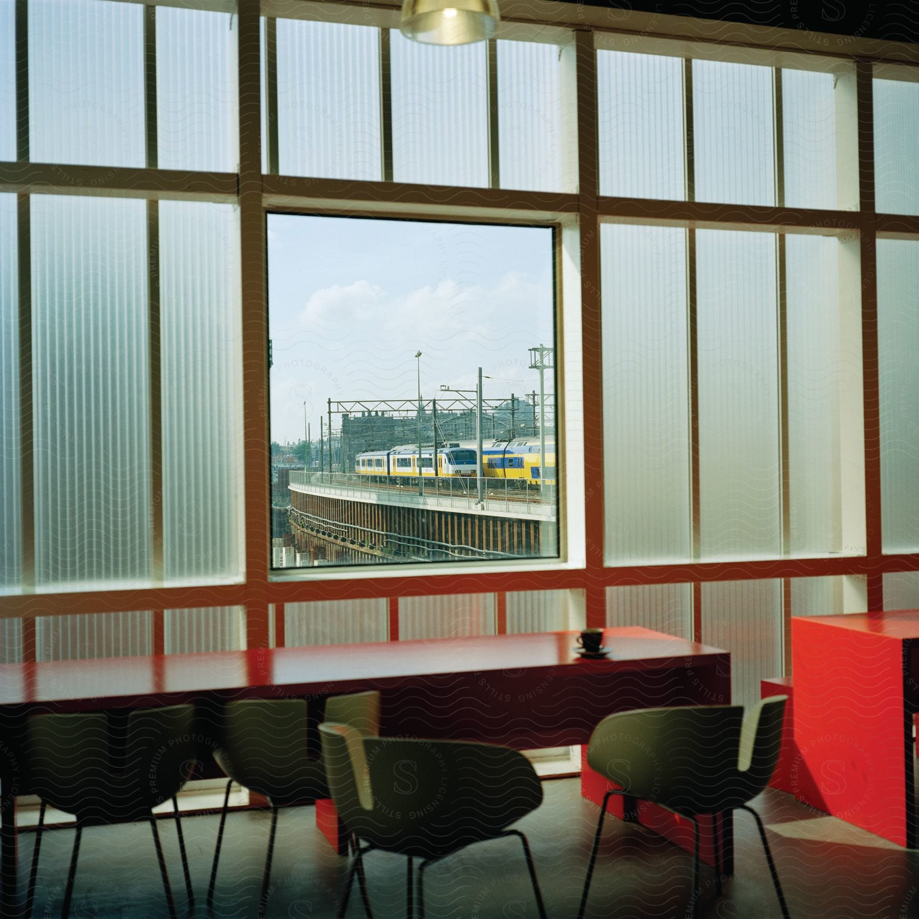 Clear window surrounded by frosted windows in room with modern decor reveals glimpse of yellow train