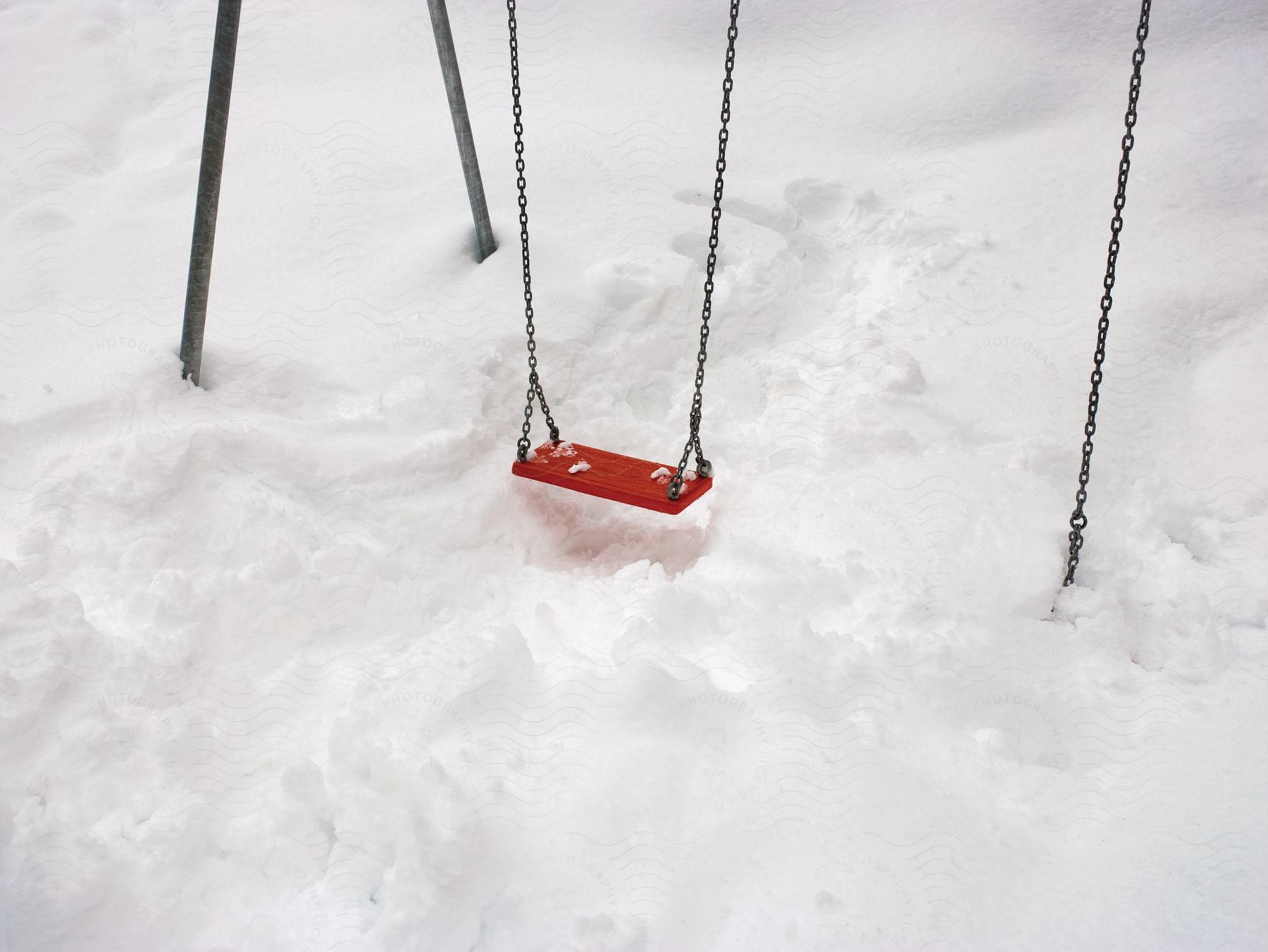 A red swing hangs over footprints in a snowcovered yard