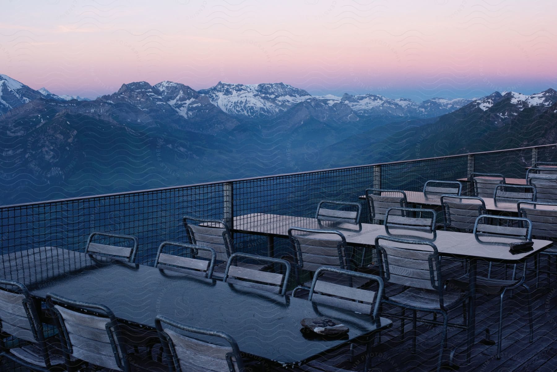 Tables and chairs on a deck next to a fence with a mountain backdrop during sunset