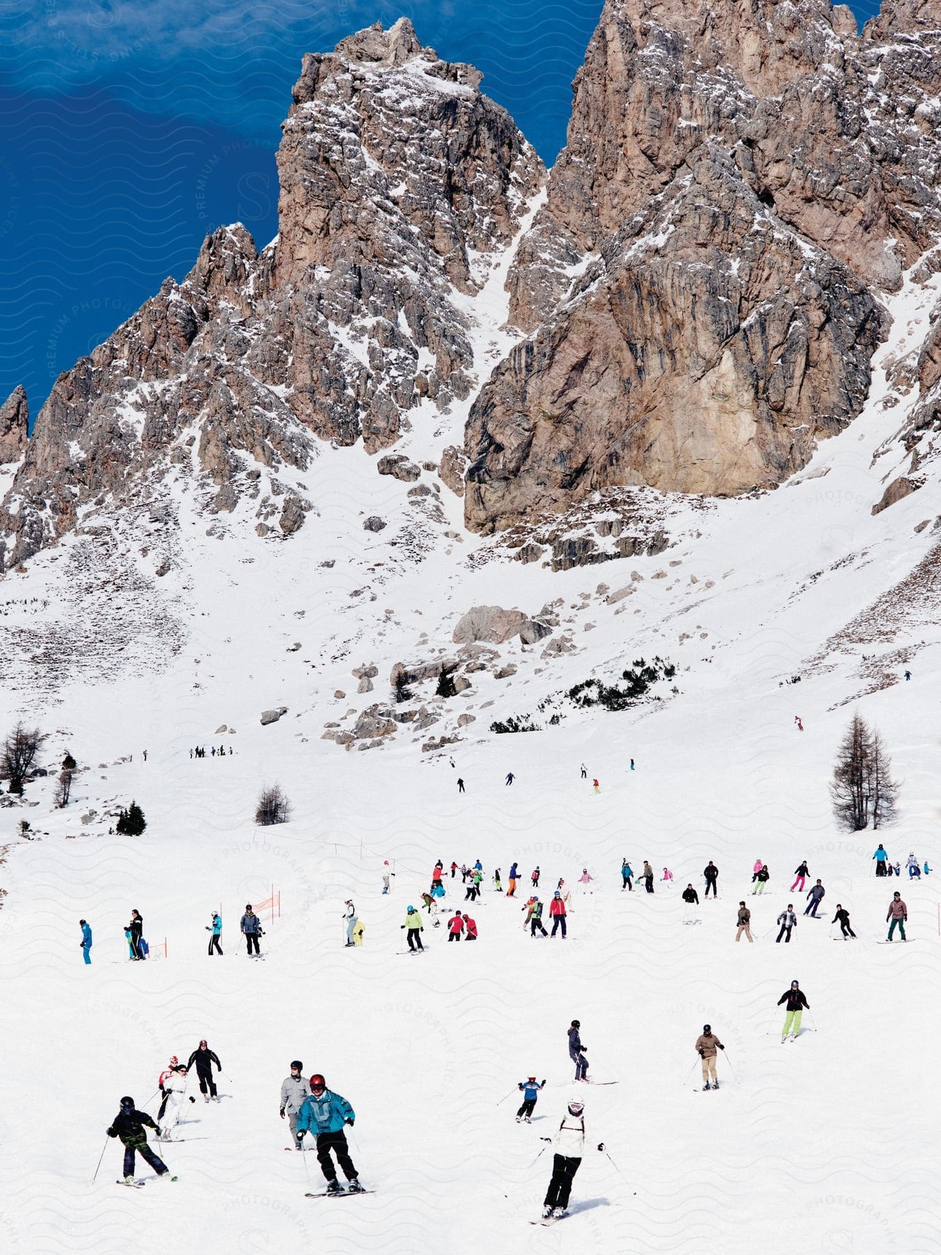 Several skiers are seen skiing in the snow below a rocky mountain