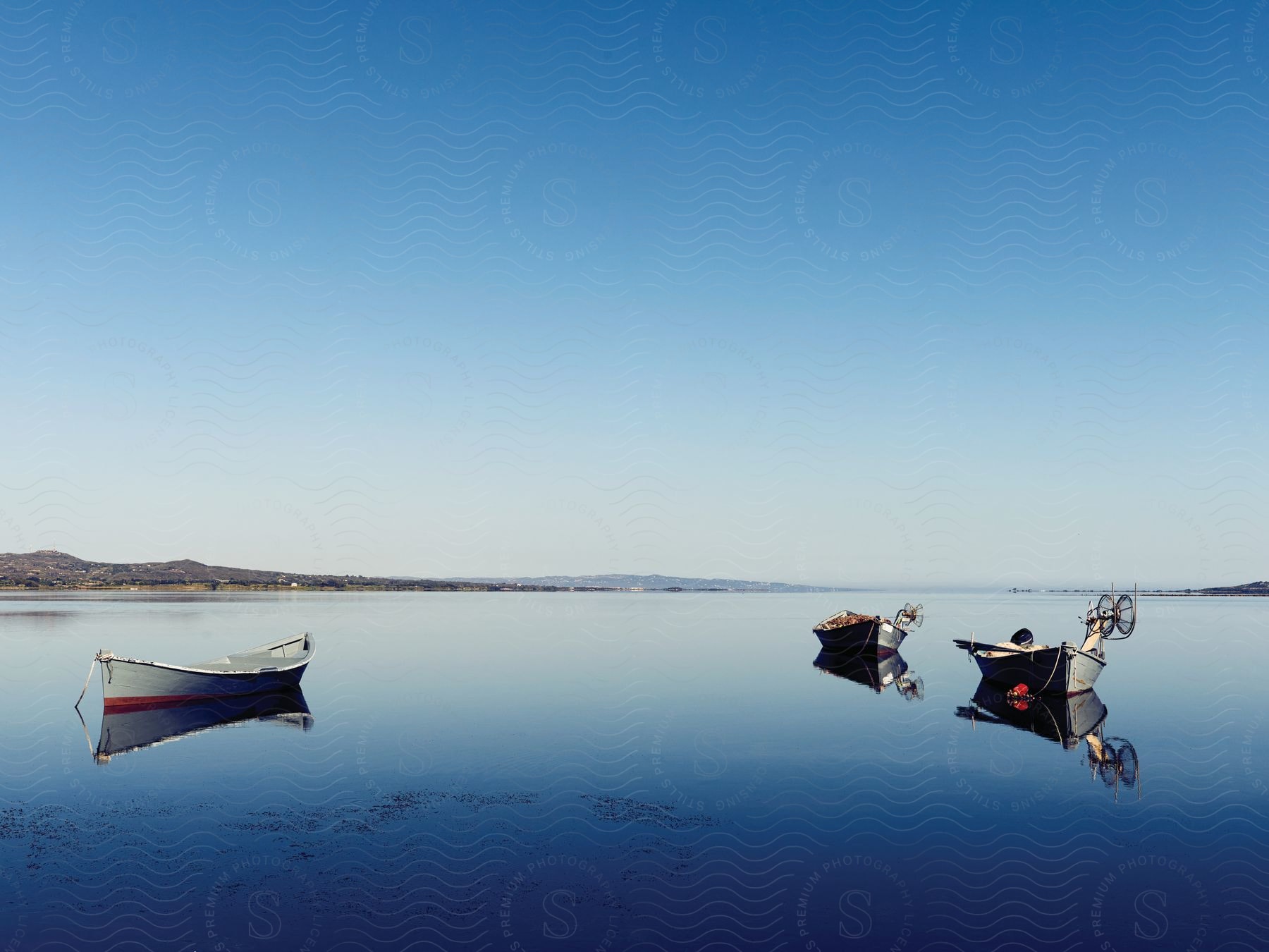 Three canoes on a flat blue lake with a clear sky in the background