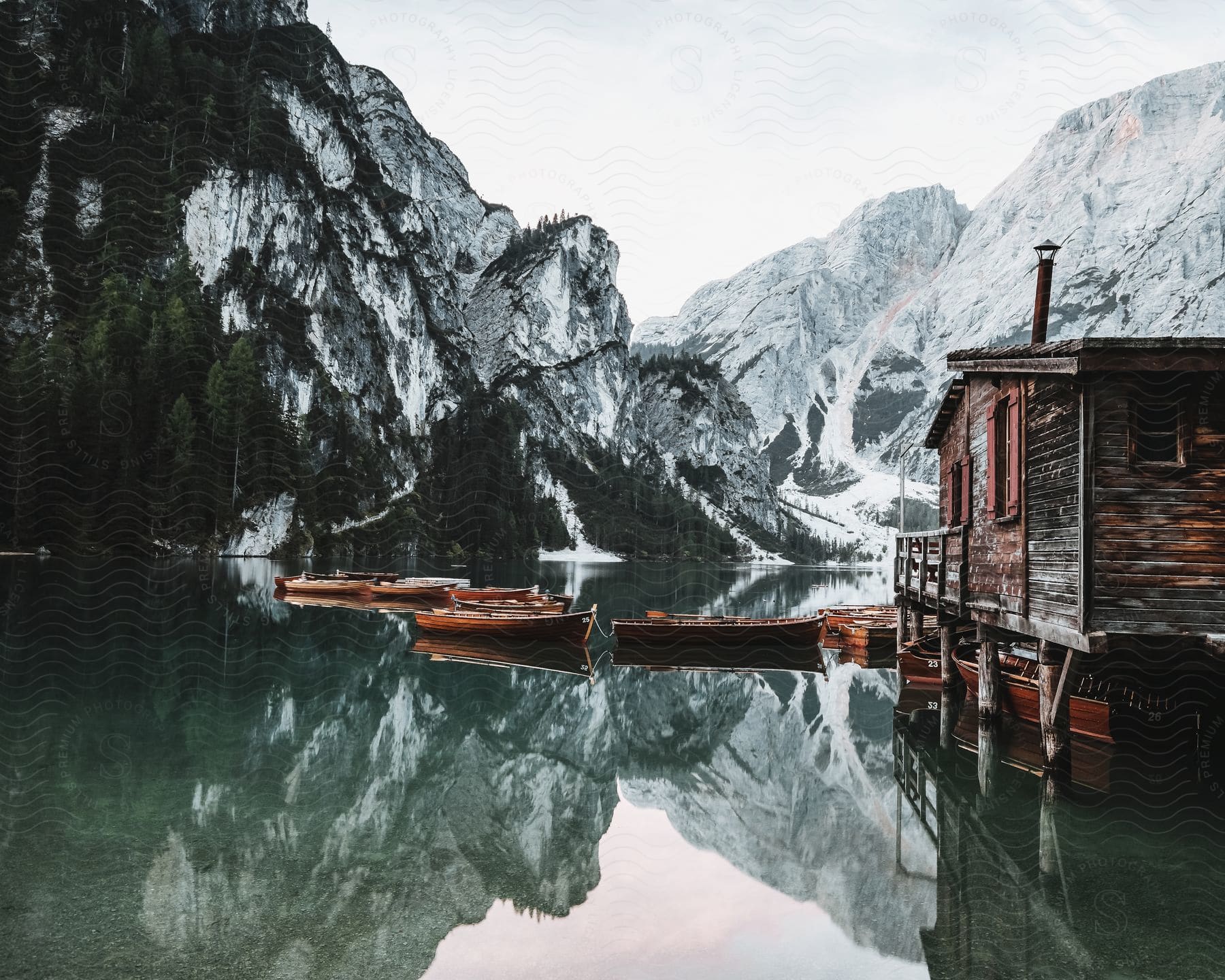 A cabin on a lake with boats moored to it and snowy mountains in the distance