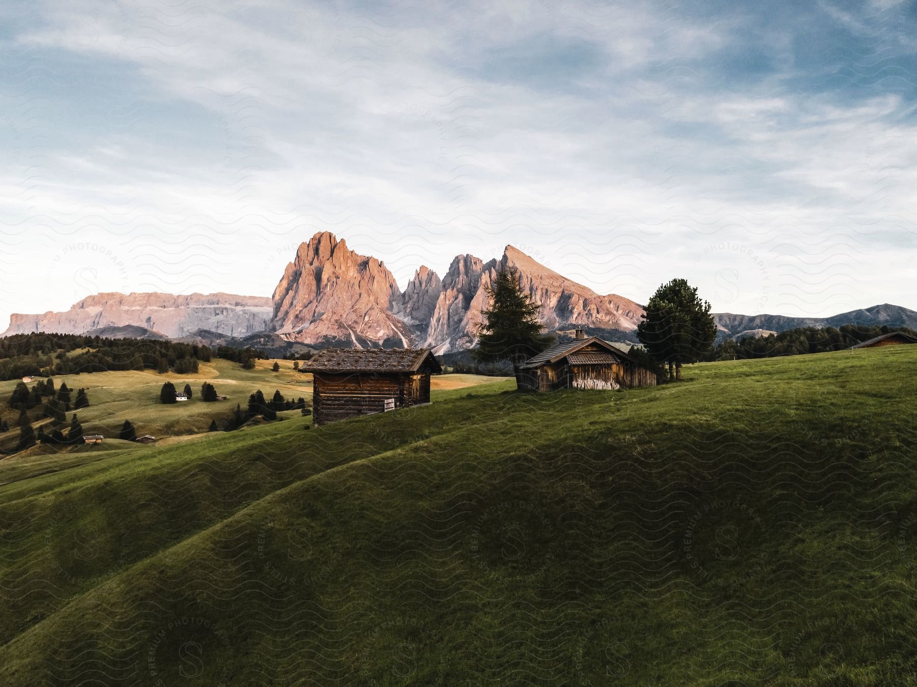 Cabins on a green hillside with the sun rising over the alps mountains