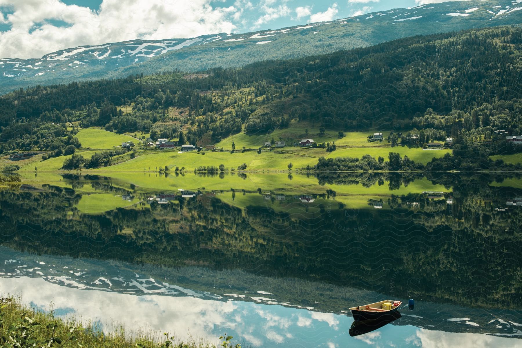 A boat floats on a lake near a rural town in the fields close to the mountains