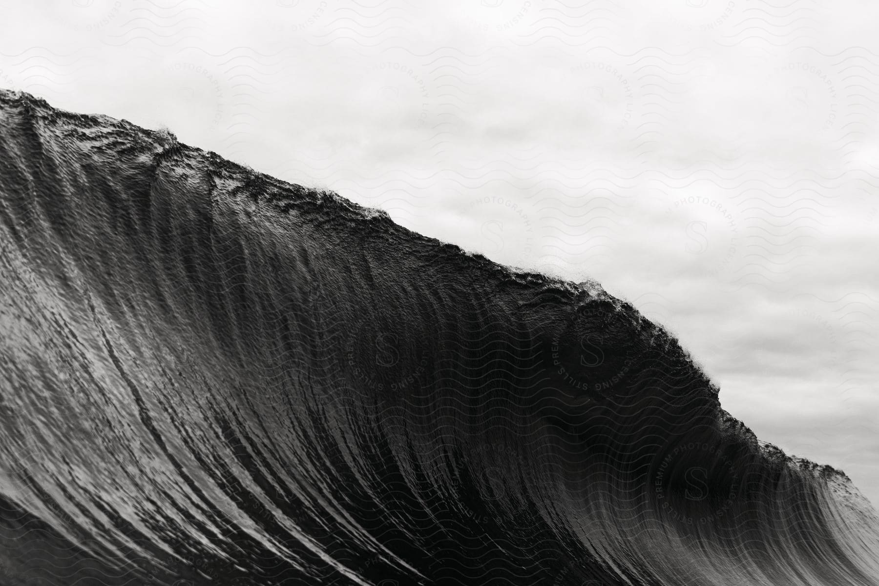 A large wave curls under a cloudy sky