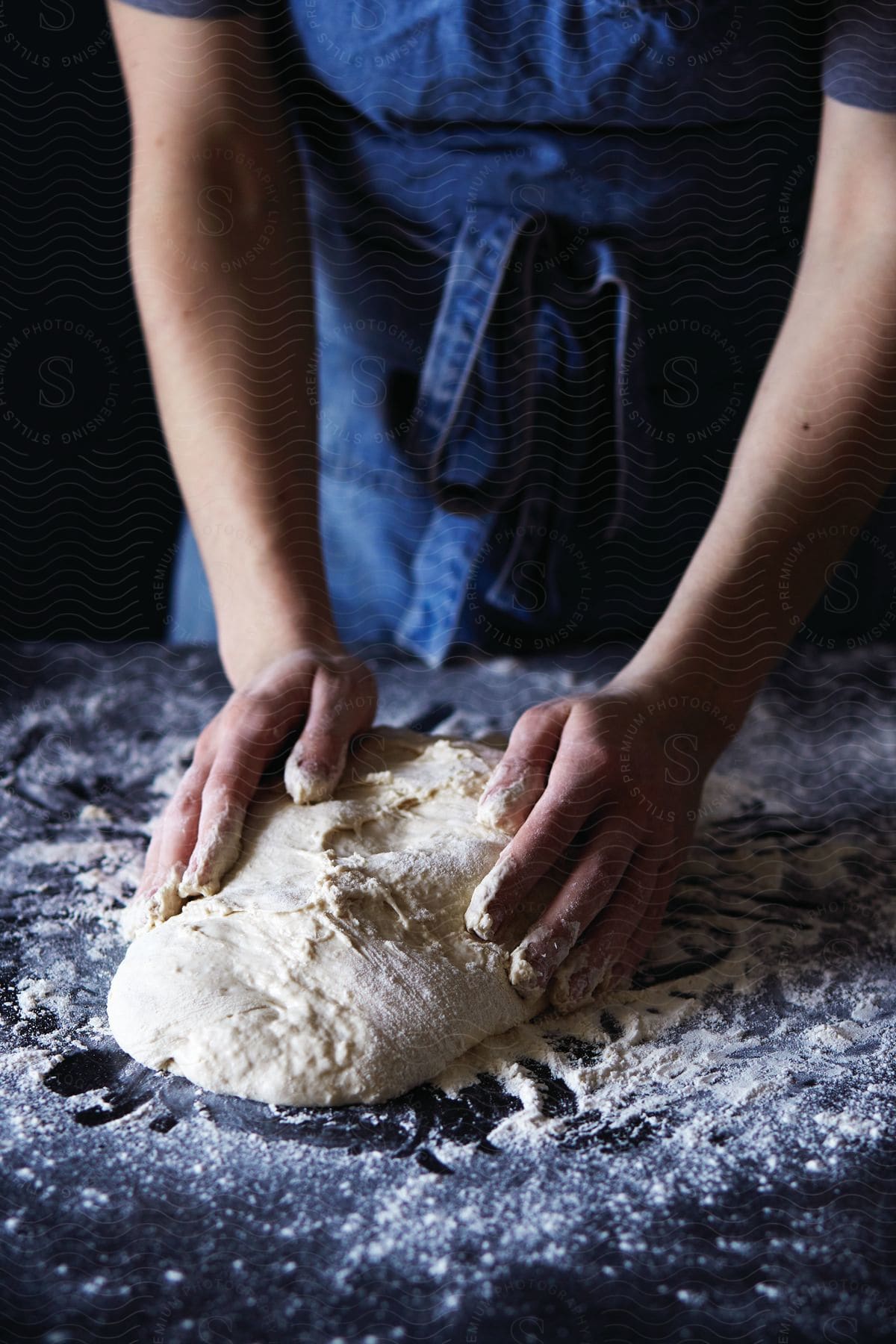 A person wearing an apron kneading dough on a countertop