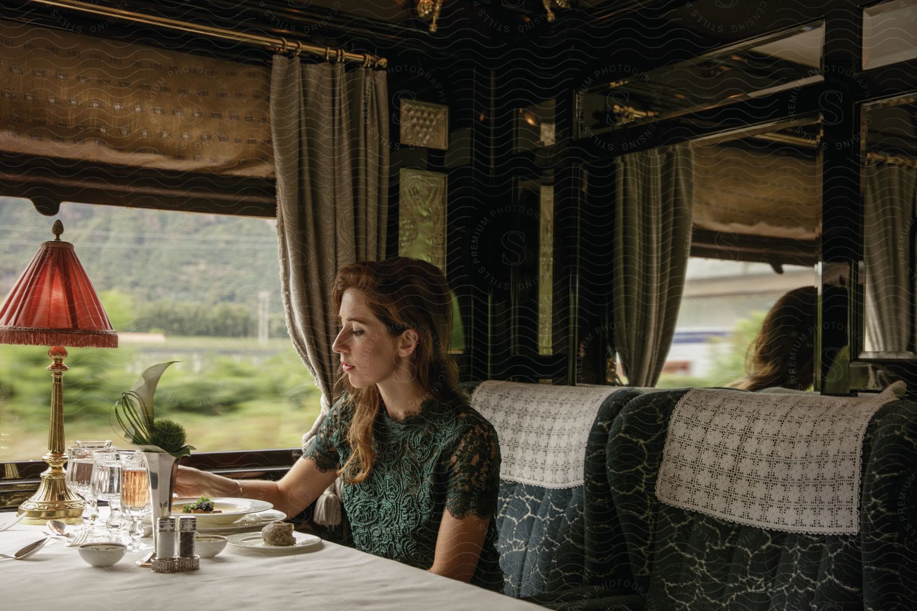 Woman in green dress eating meal in fancy train car passing countryside