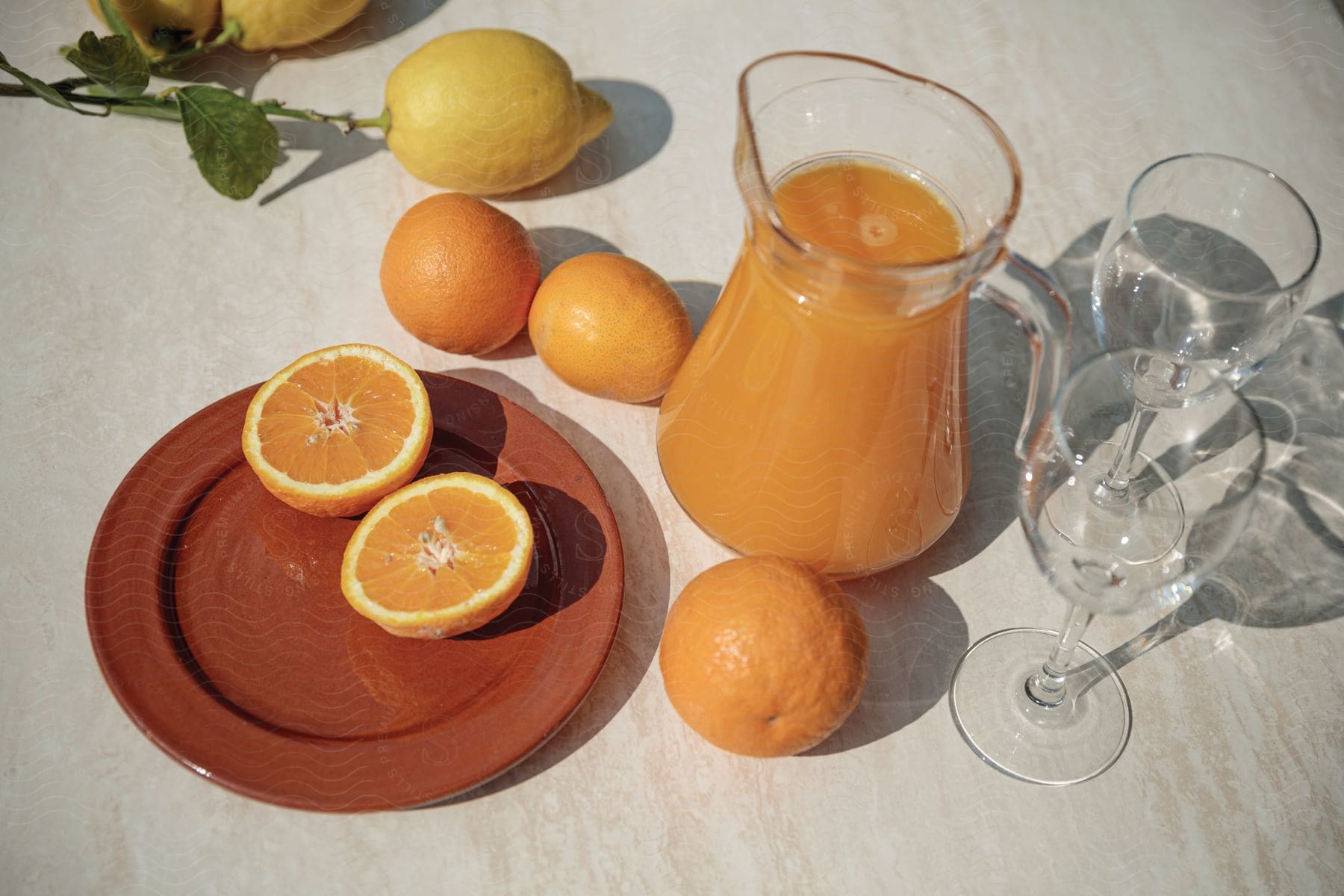 A pitcher of orange juice is surrounded by oranges lemons and tableware