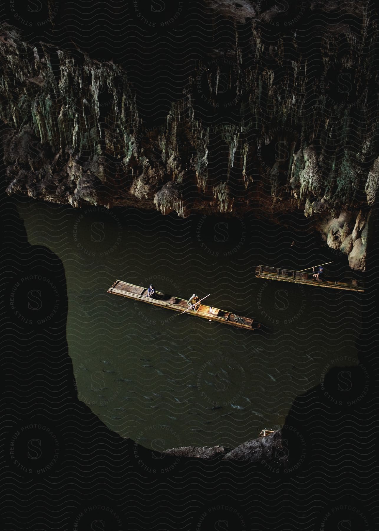Two rafts with three people floating on the water inside a large cave