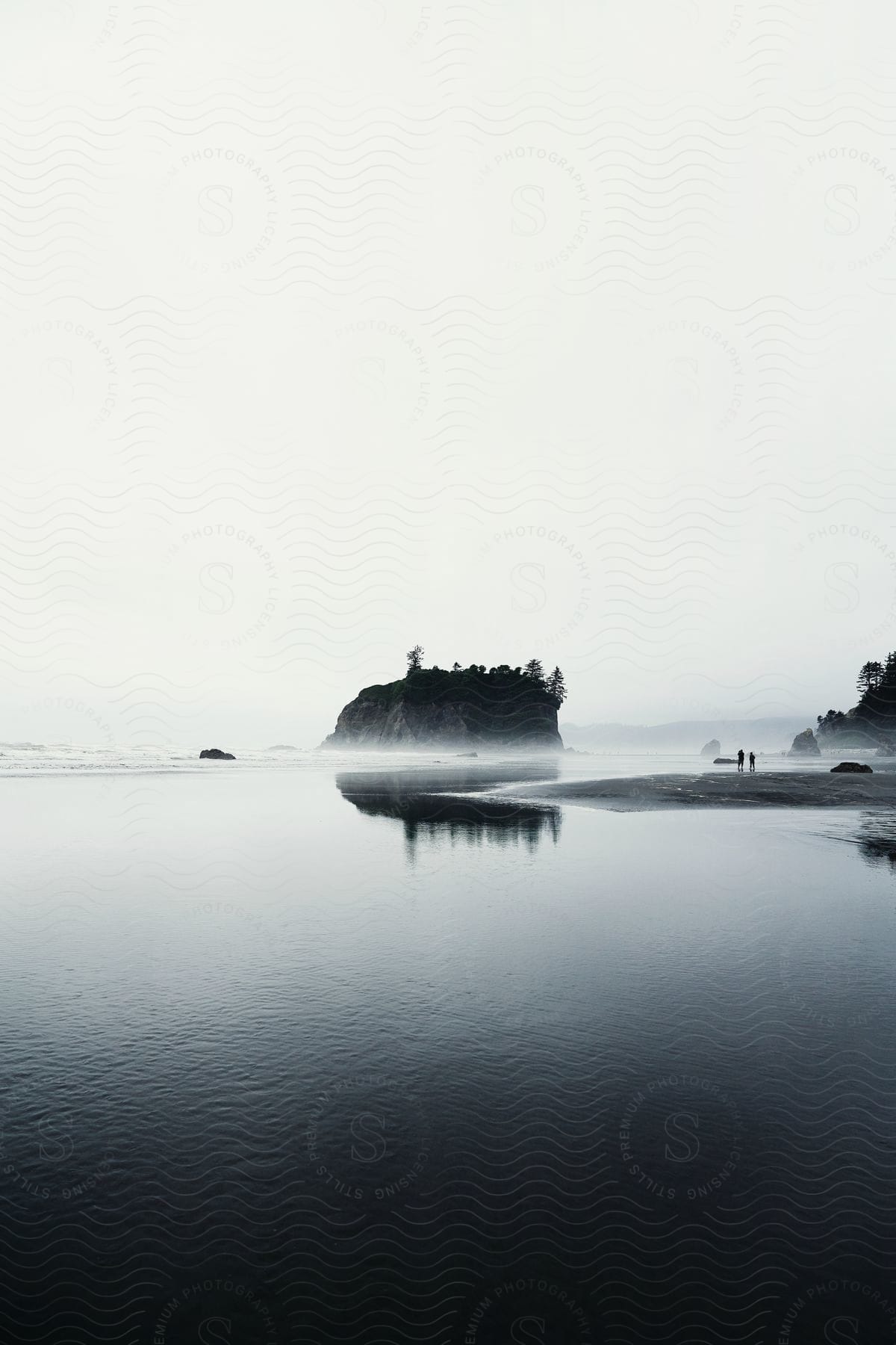 A small land mass with two people standing near the shore in the ocean