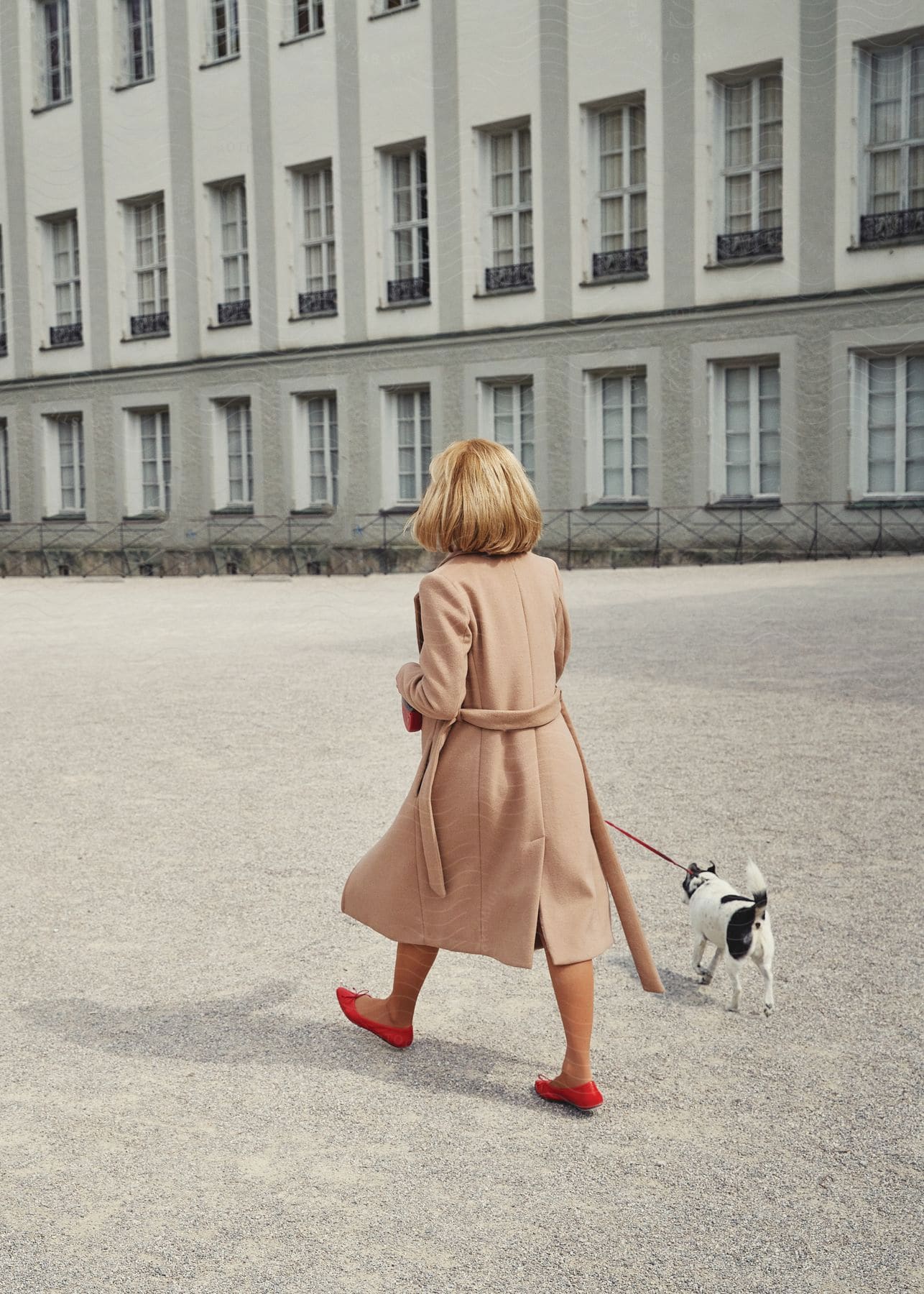 A woman walking her small dog in front of a building