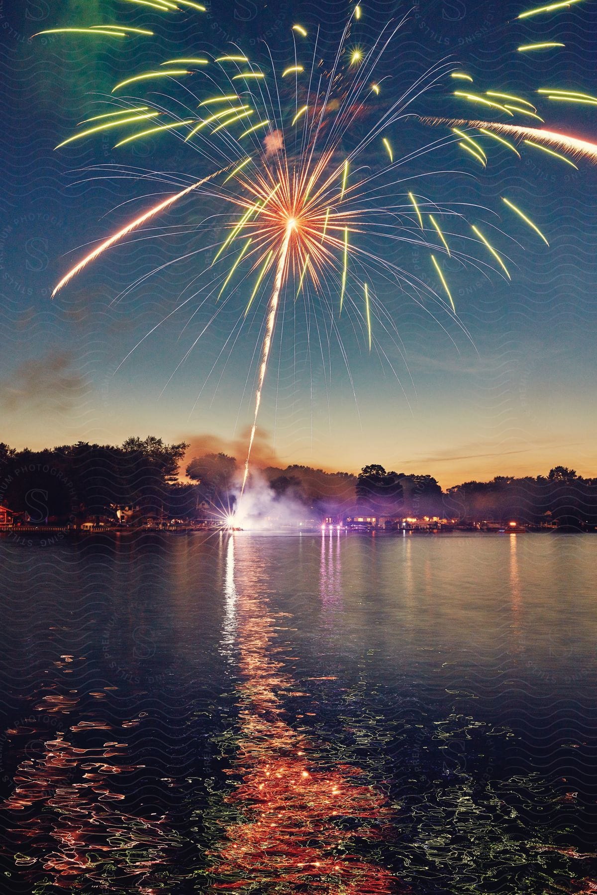 Fireworks explode over the water at night as lights reflect colors on the surface