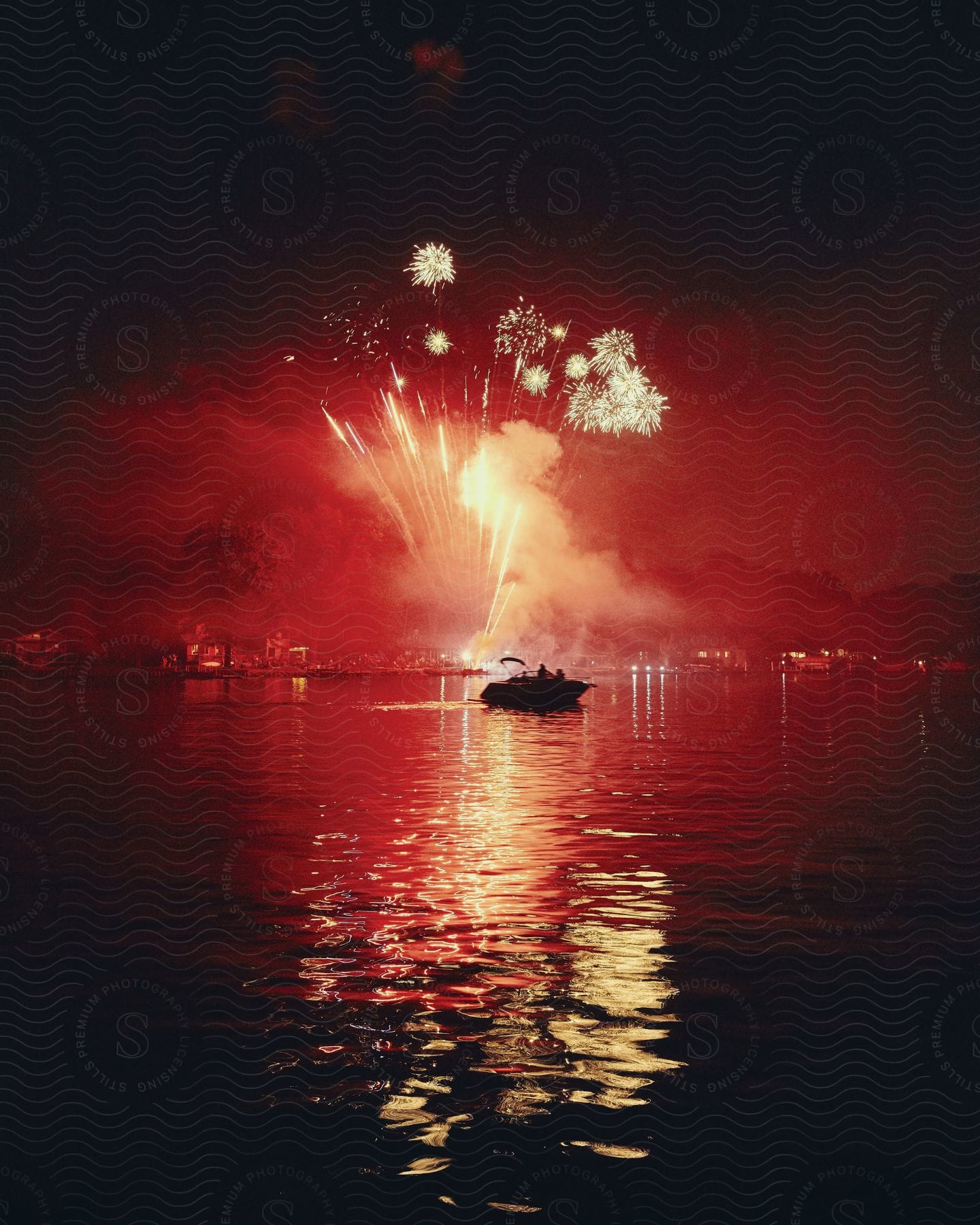 A boat on the water at night with red fireworks in the background