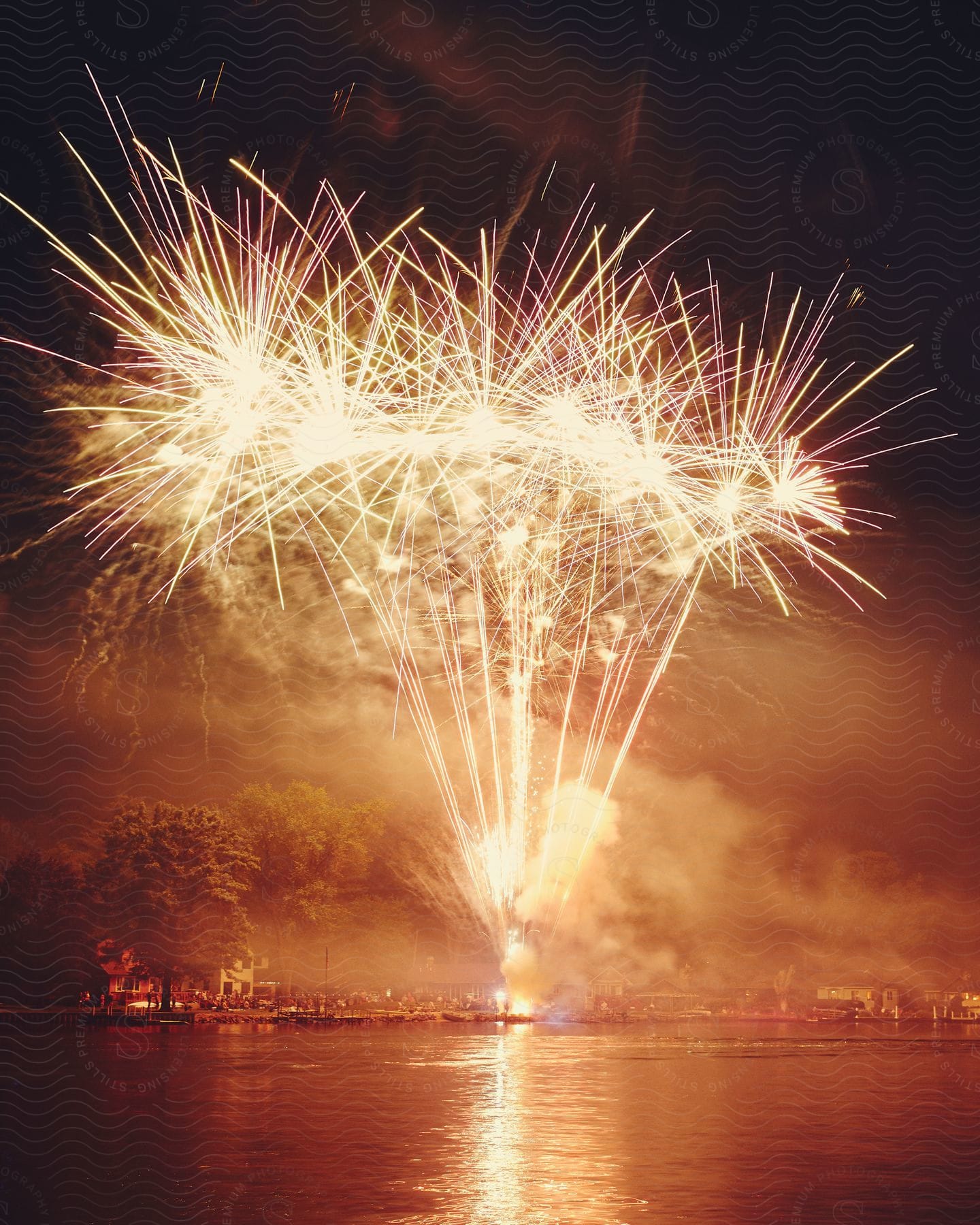 Fireworks illuminate the night sky over water creating a smoky atmosphere near the city waterfront