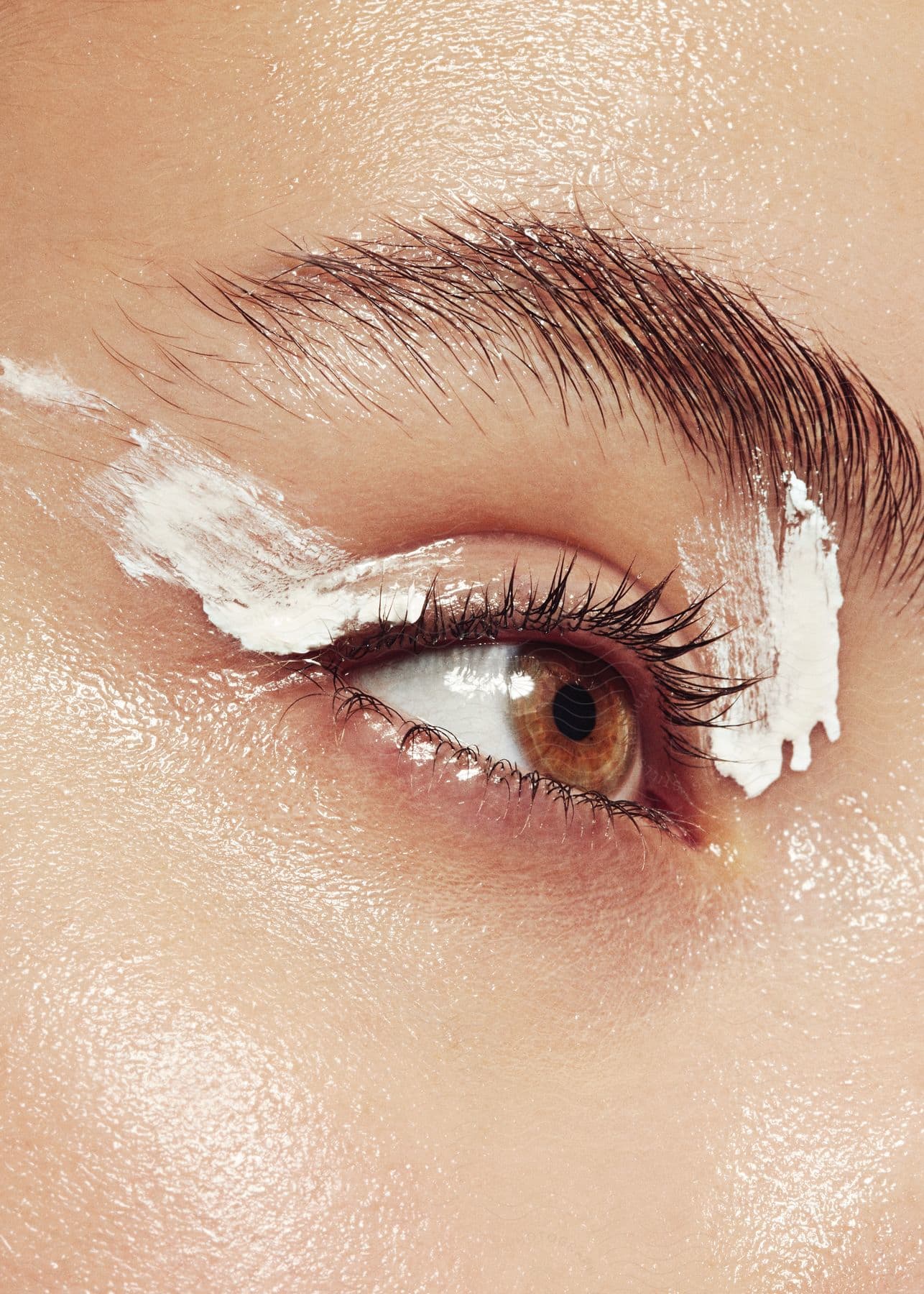 A womans eye with white cream on two points of the eyelid