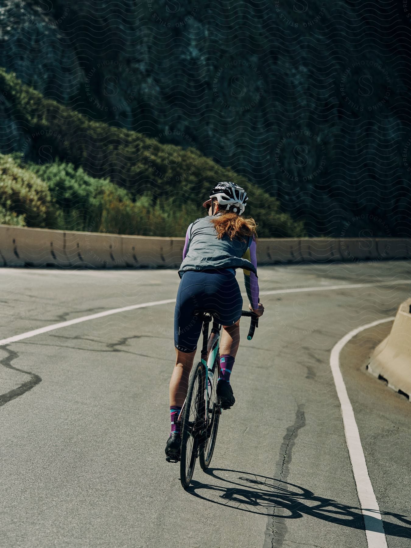 A woman rides a bicycle on a highway near a mountain
