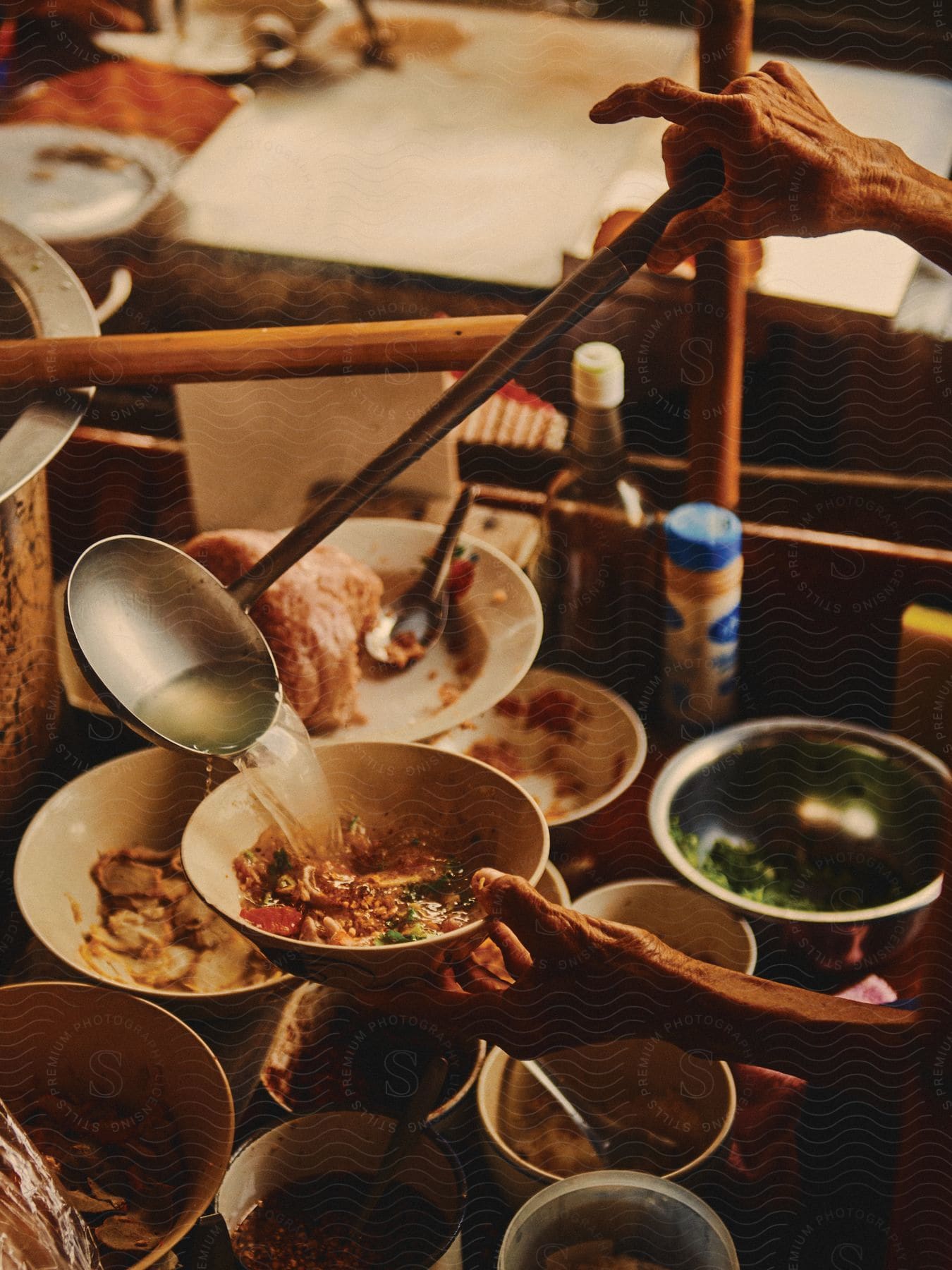 A chef pours broth onto a bowl next to containers of various foods and ingredients