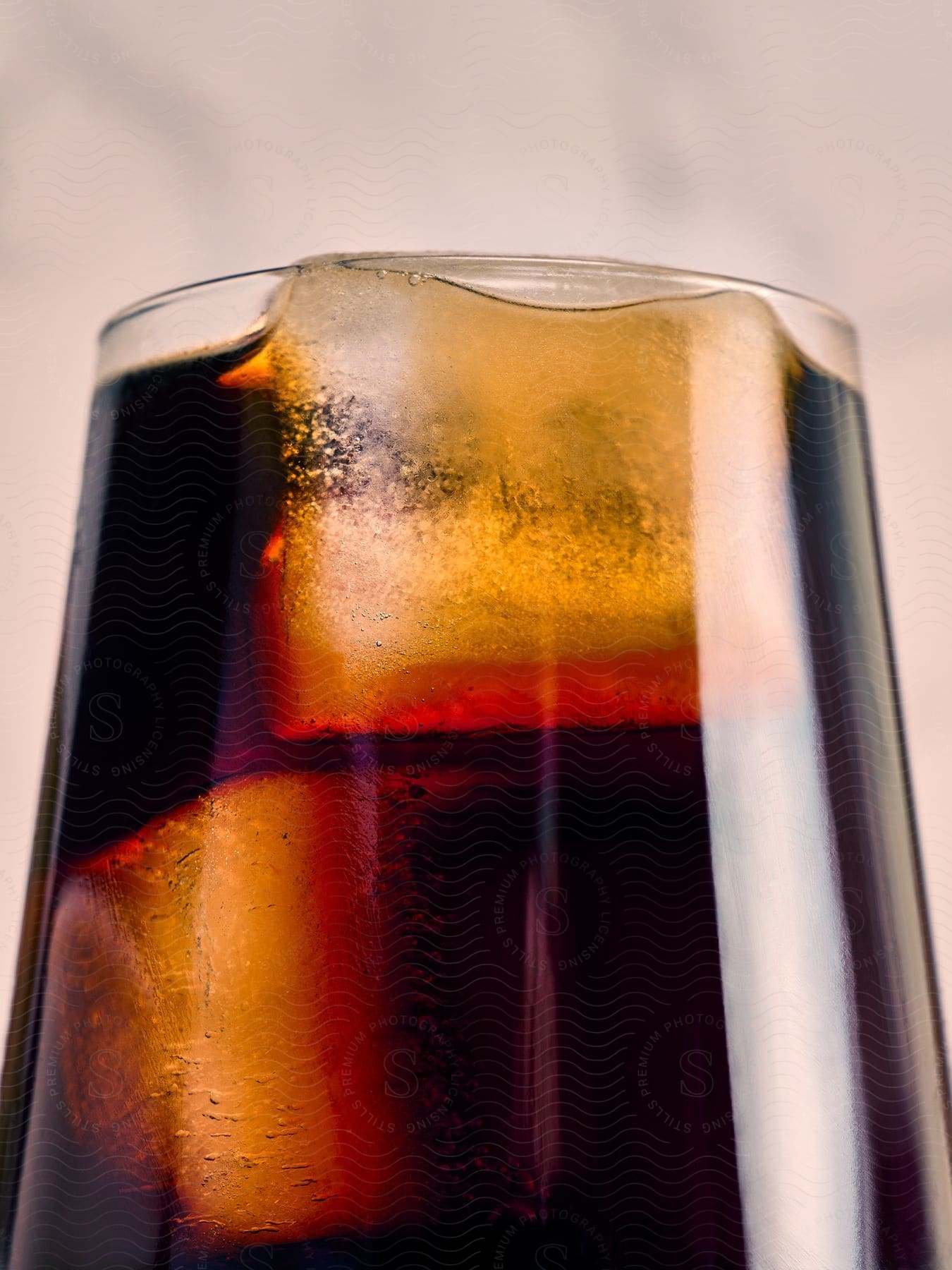 A glass of cola filled to the brim with a couple ice cubes in it