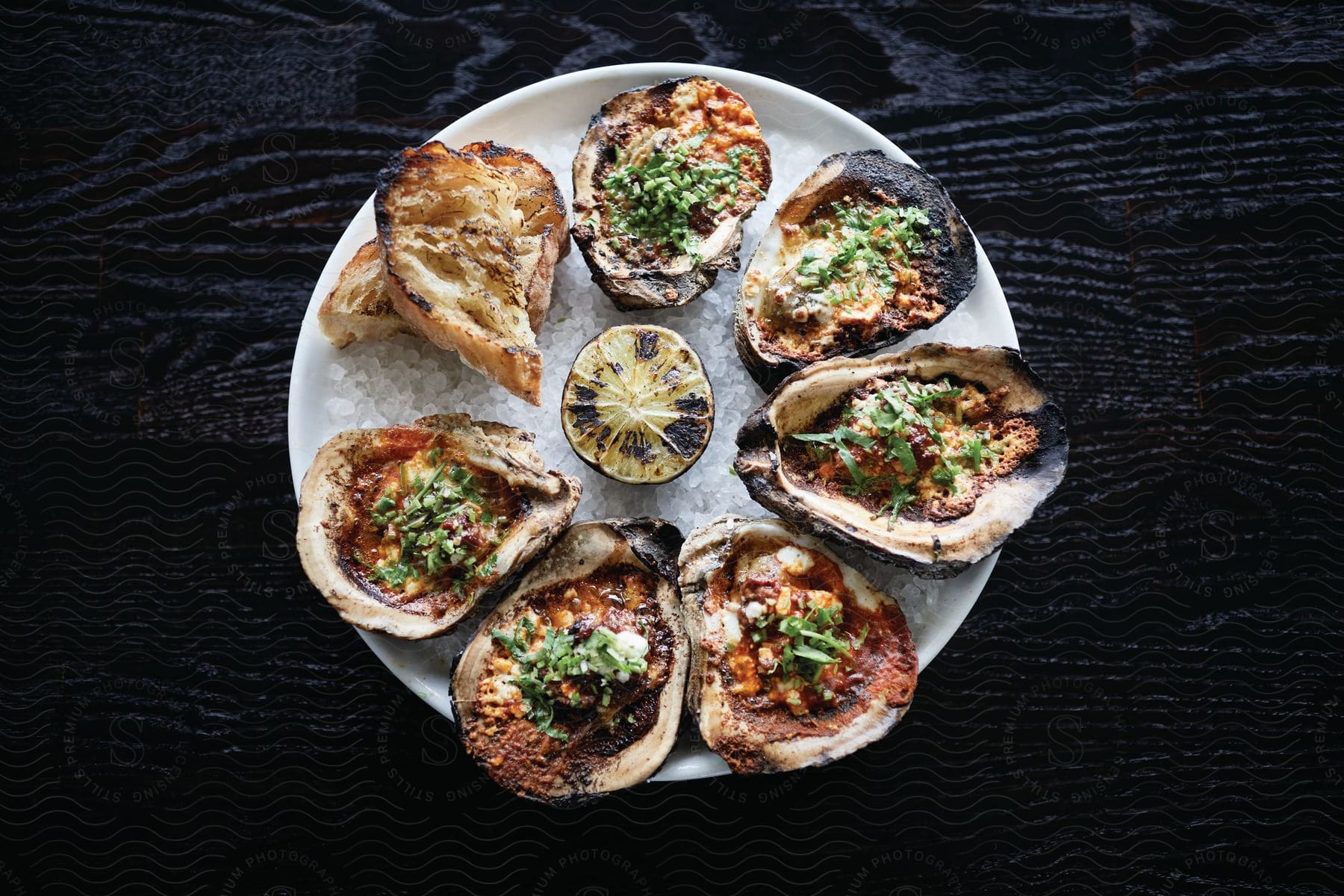 Cooked oysters arranged in a circle on a white plate on a black table