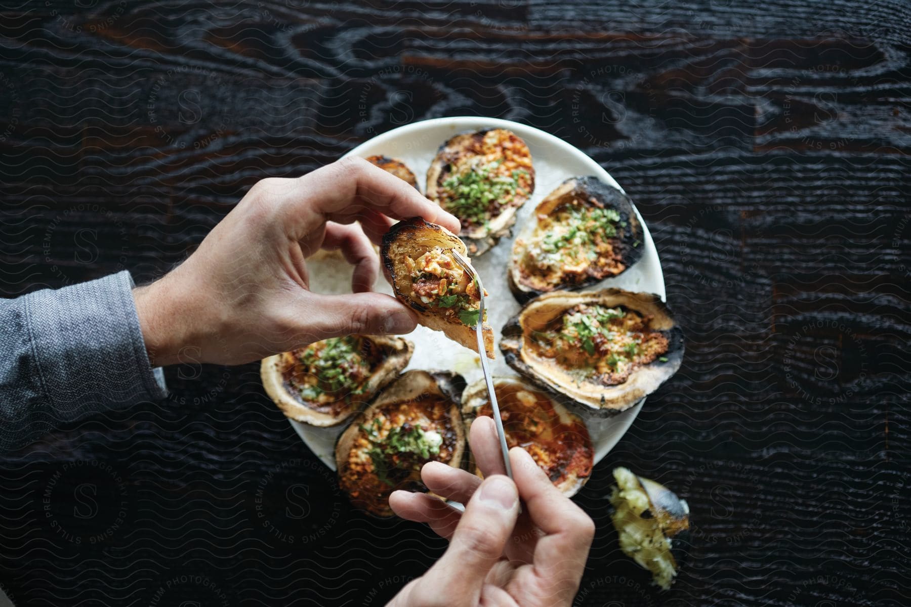 Stock photo of a person holding a grilled oyster with a fork ready to eat