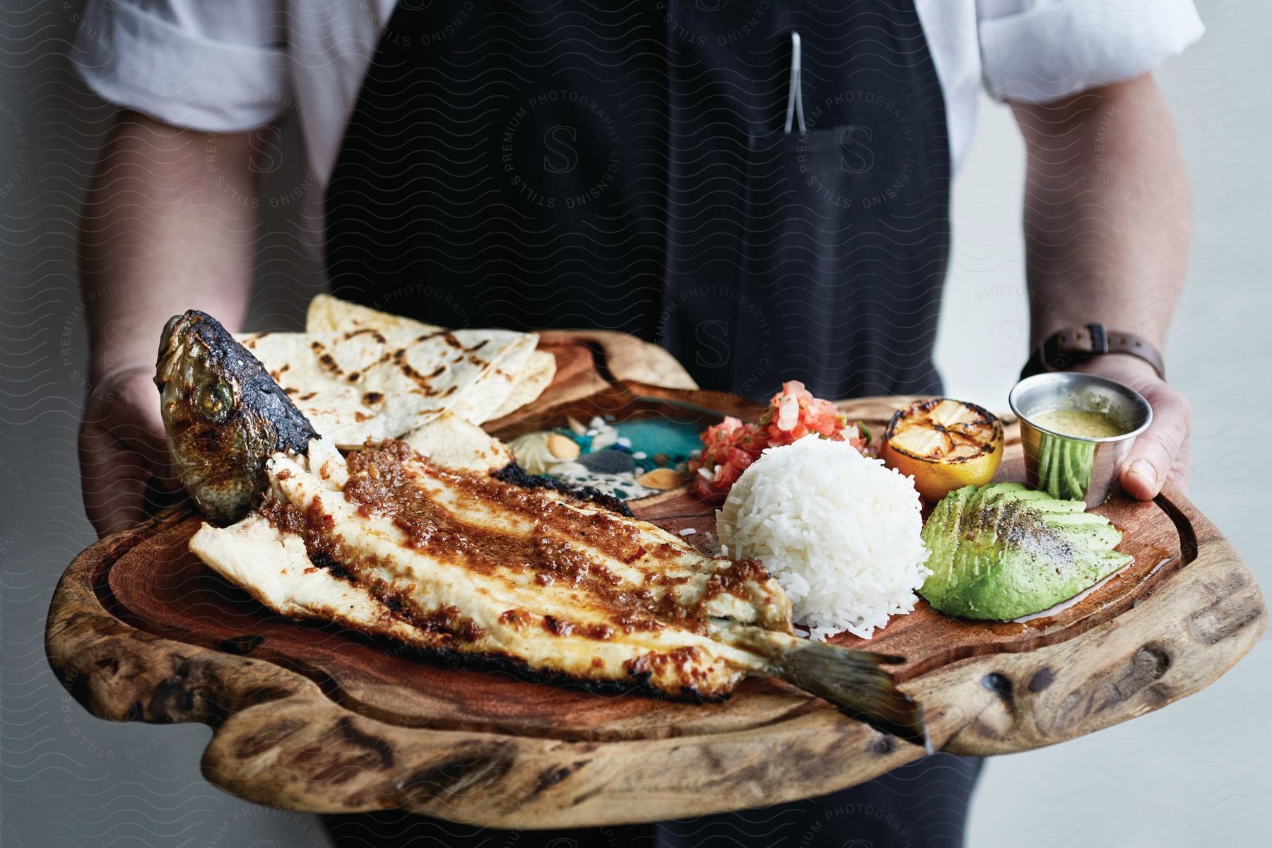 A waiter carries a wooden tray with fried fish and side dishes