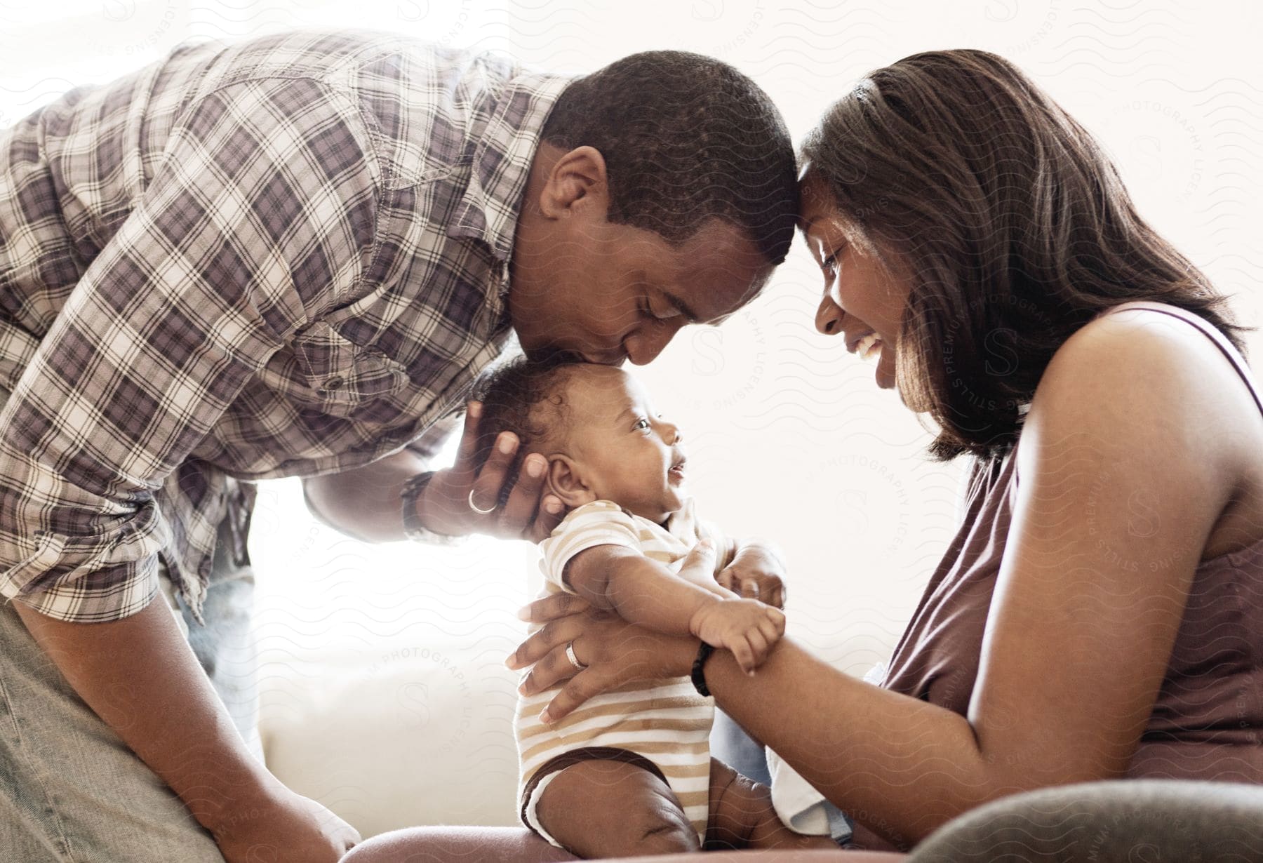 A family with a mother holding a baby and a father kissing its head