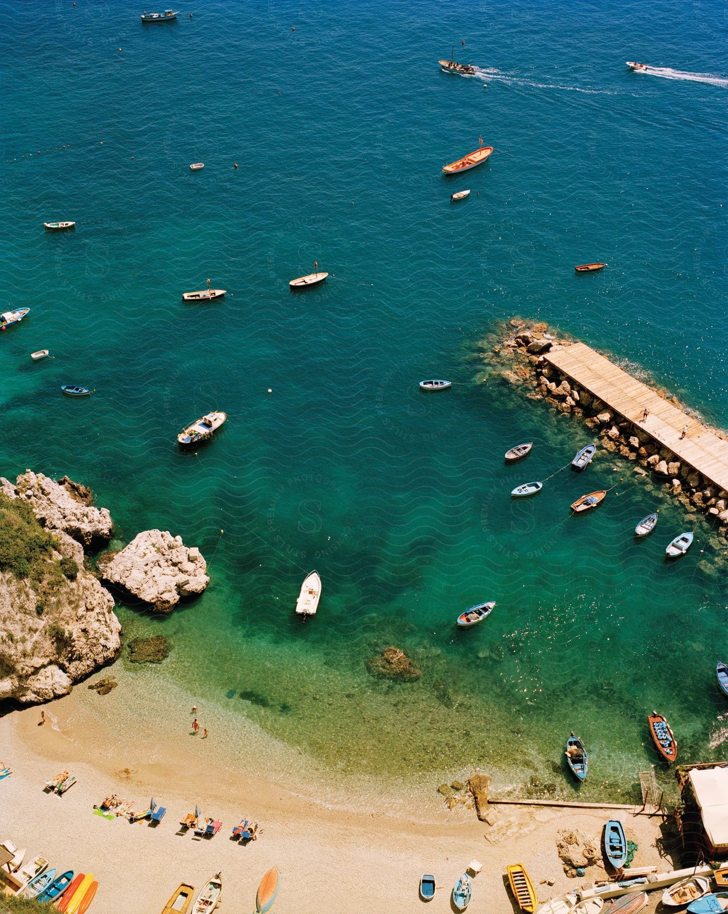 Stock photo of people enjoying a beach with clear water and several boats on a sunny summer day