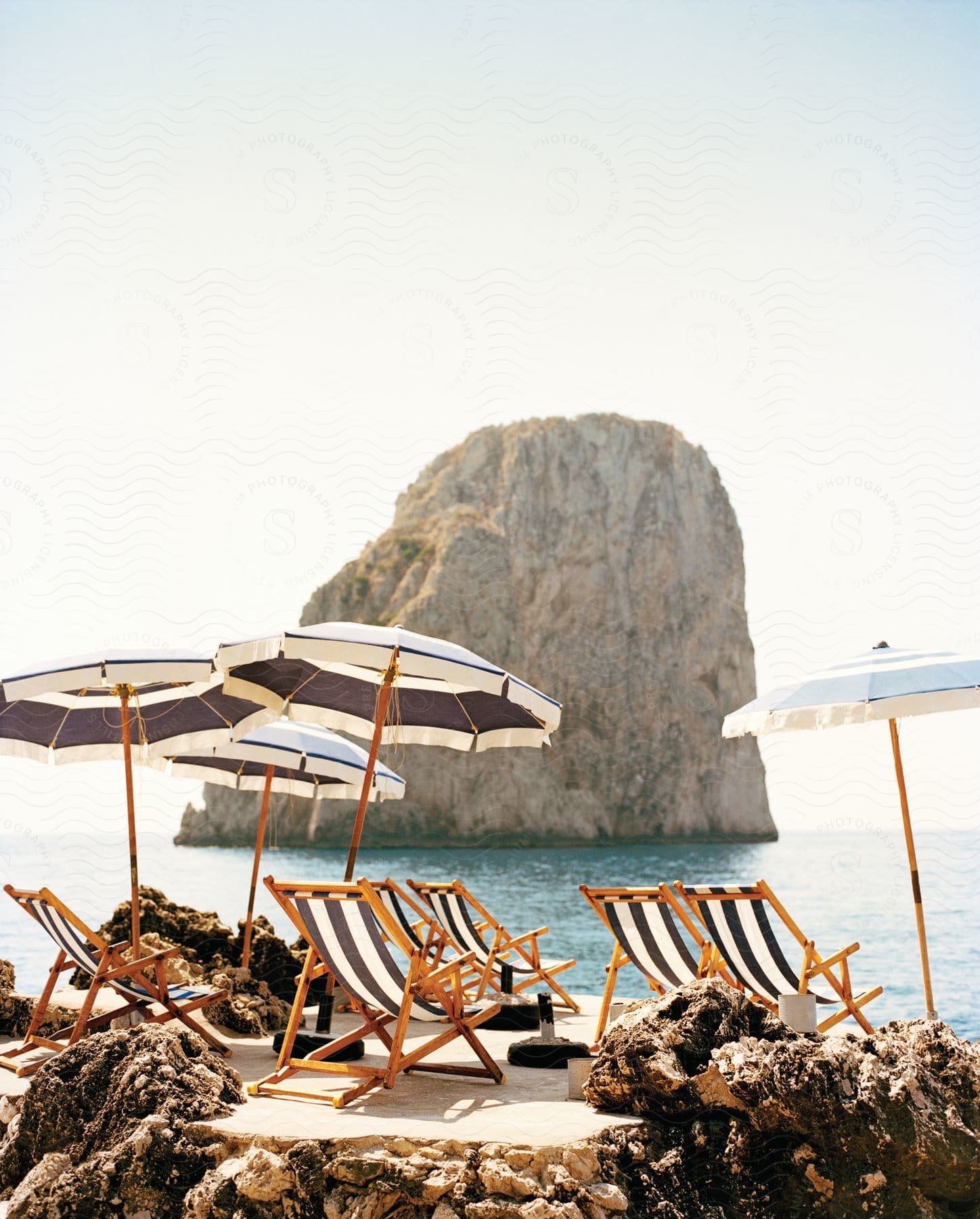 A sunny beach with chairs umbrellas and a rocky hill in the background