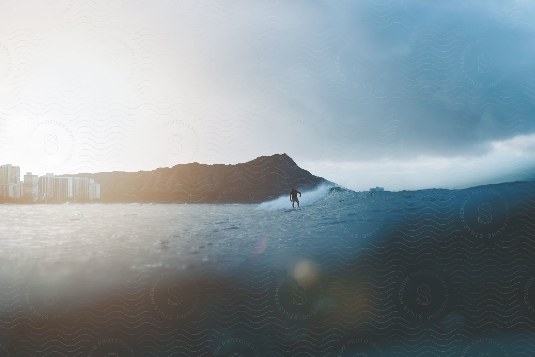 A person surfing a wave with a cliff and buildings in the background